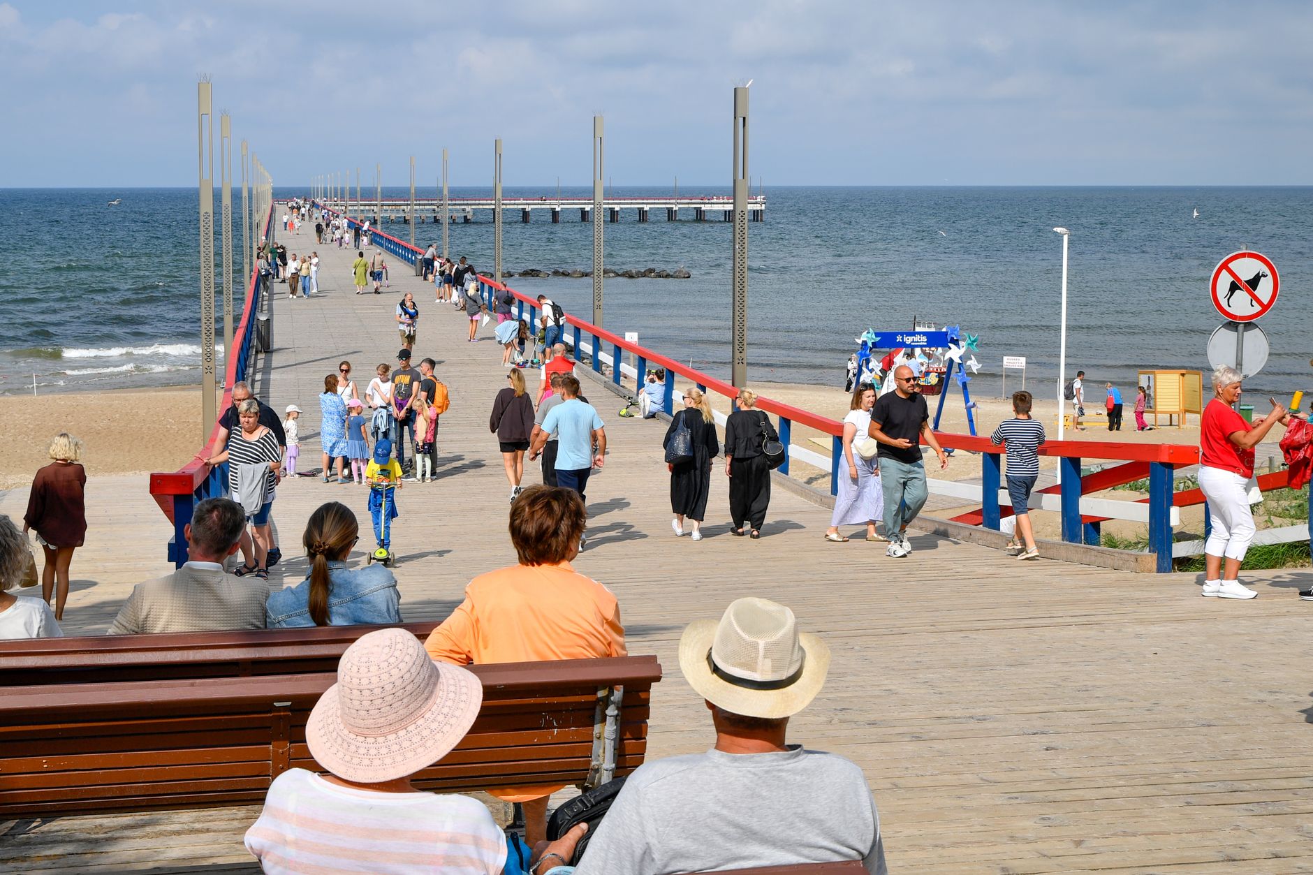 People strolling along Palanga pier in Lithuania under bright summer skies.