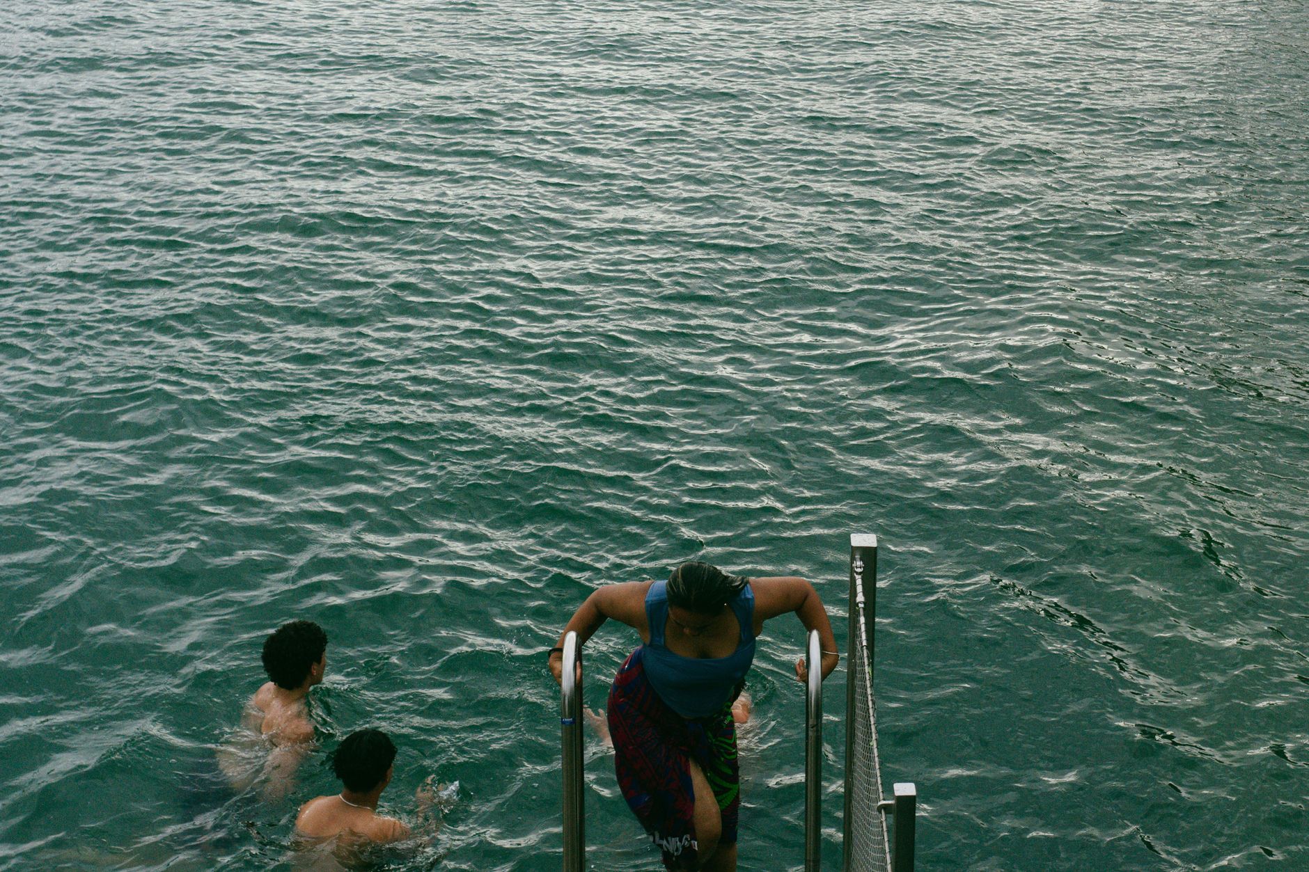Group of people enjoying a swim in open water with one using a ladder to exit.