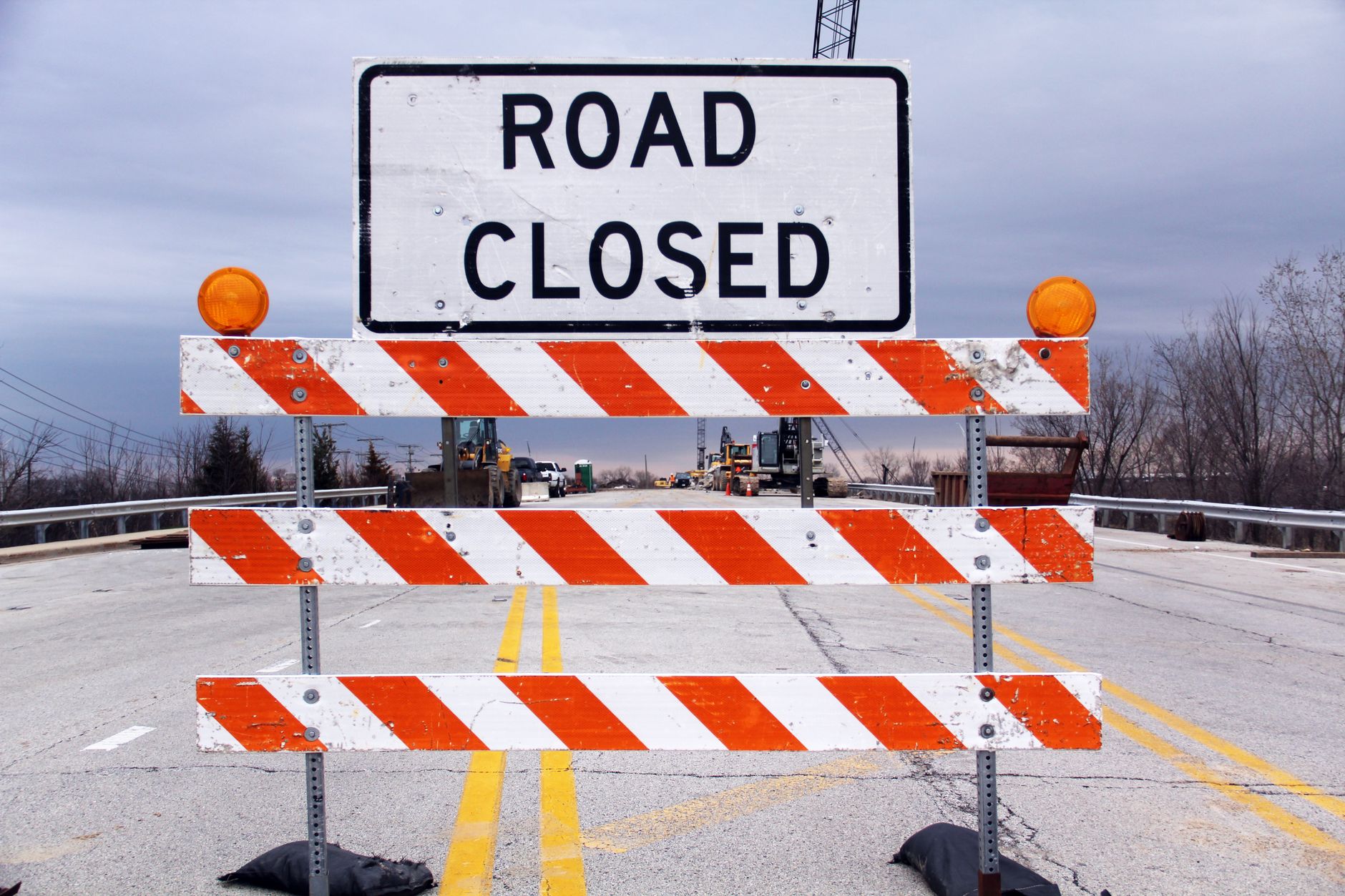 A road closed sign with barricade highlights caution on a suburban highway.