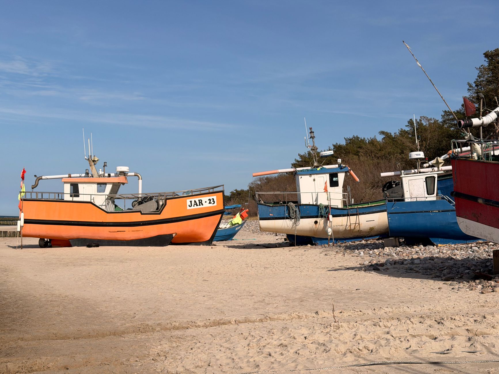 Colorful fishing boats on the sandy beach of Jarosławiec, Poland under a clear blue sky.