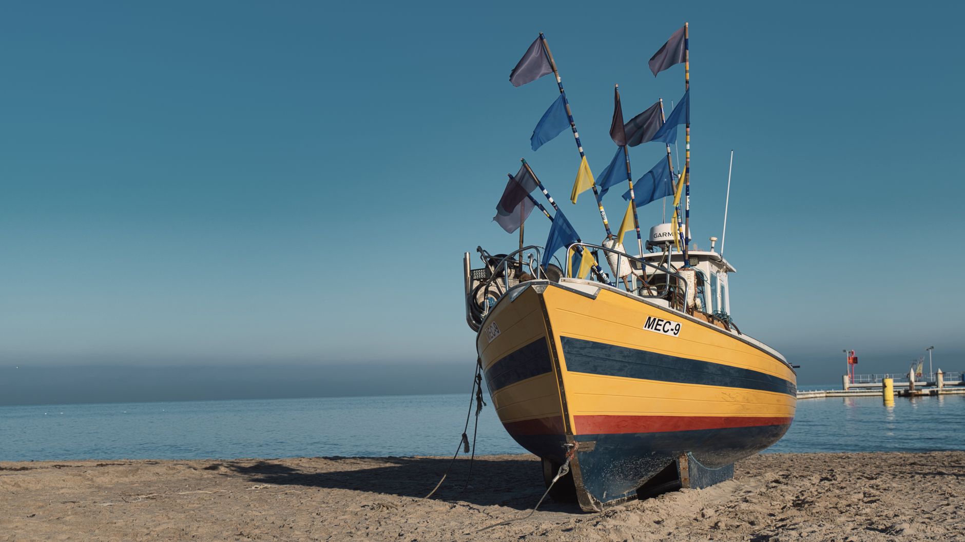 Vibrant fishing boat with flags on a sunny beach in Gdynia, Poland.