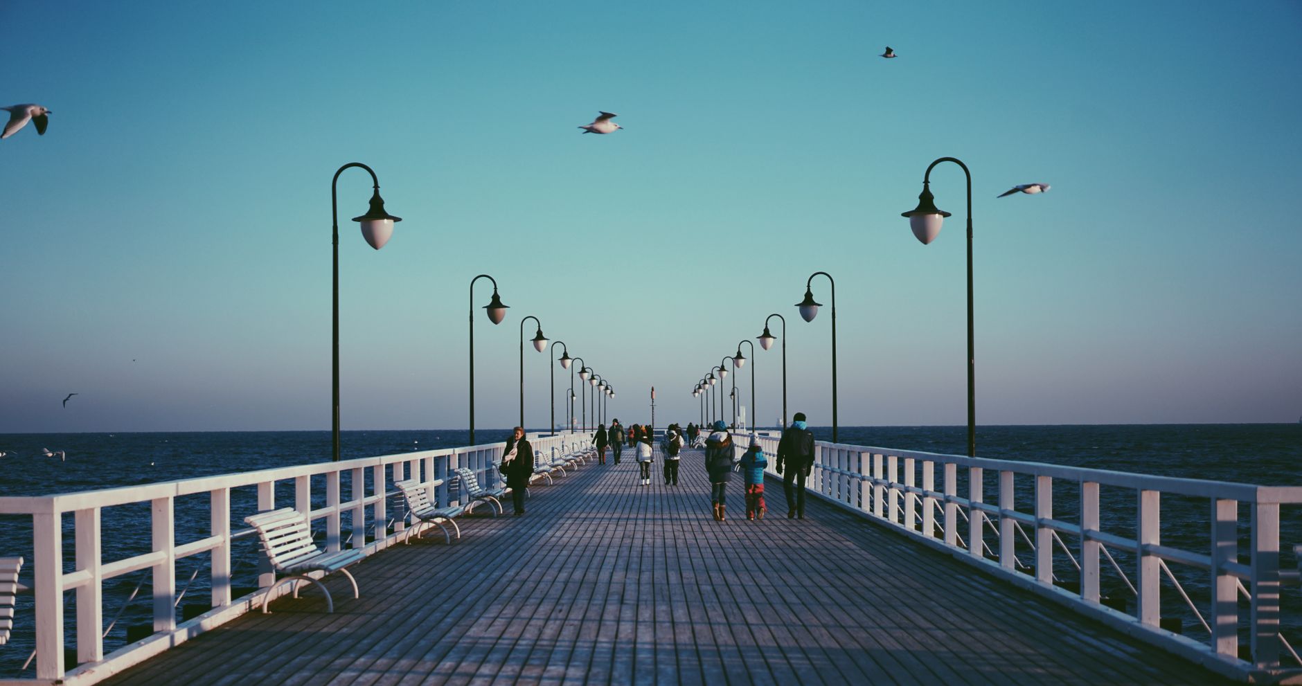 A peaceful pier in Gdynia, Poland with people strolling and seagulls flying at sunset.