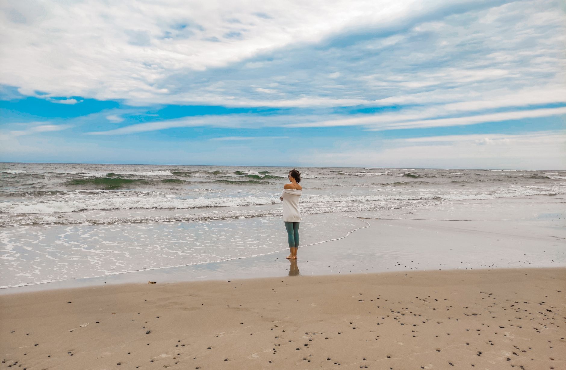 A woman stands peacefully by the Baltic Sea in Łeba, Poland during the daytime.
