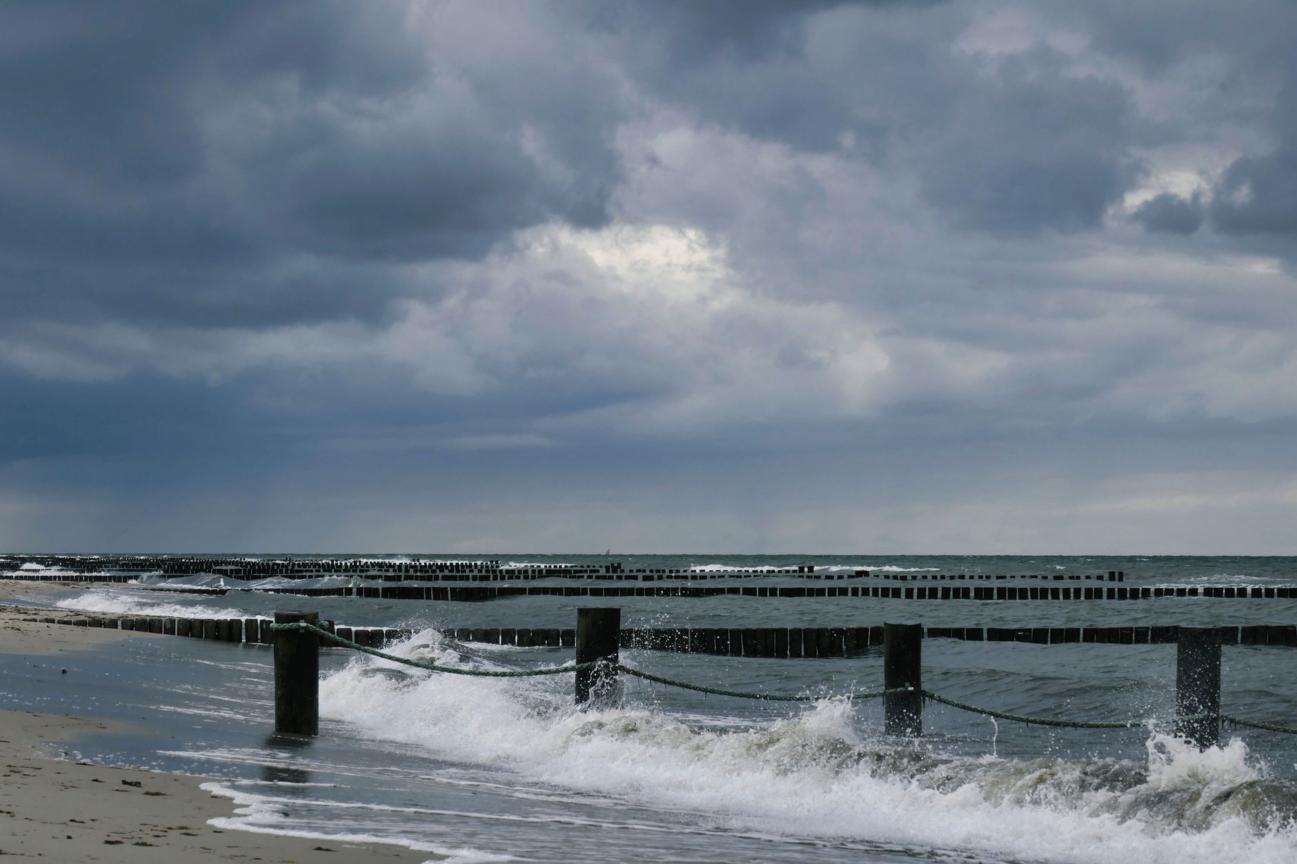 Stormy Baltic Sea waves with wooden posts on Kühlungsborn beach under cloudy skies.