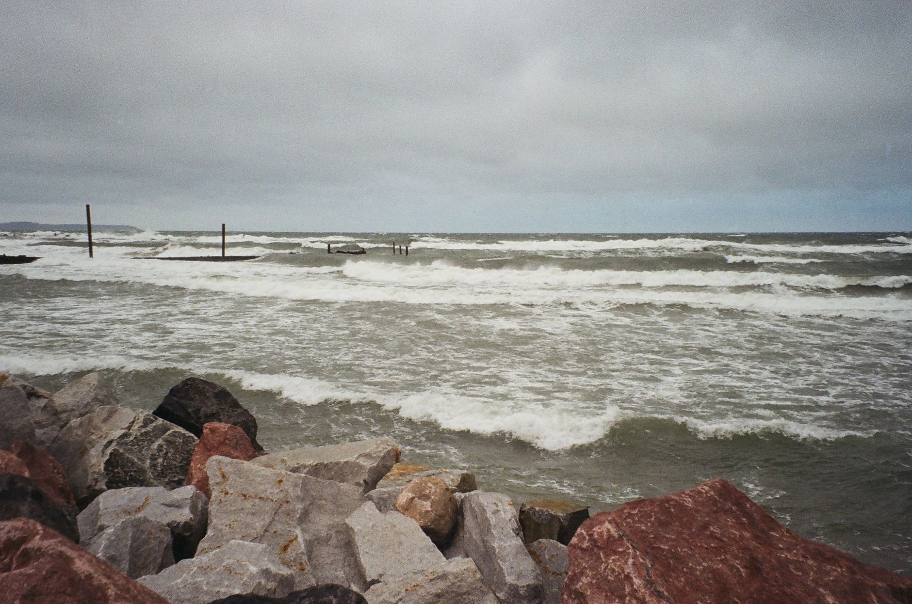 Waves crashing against the rock-strewn shoreline of Svetlogorsk, Russia under a cloudy sky.