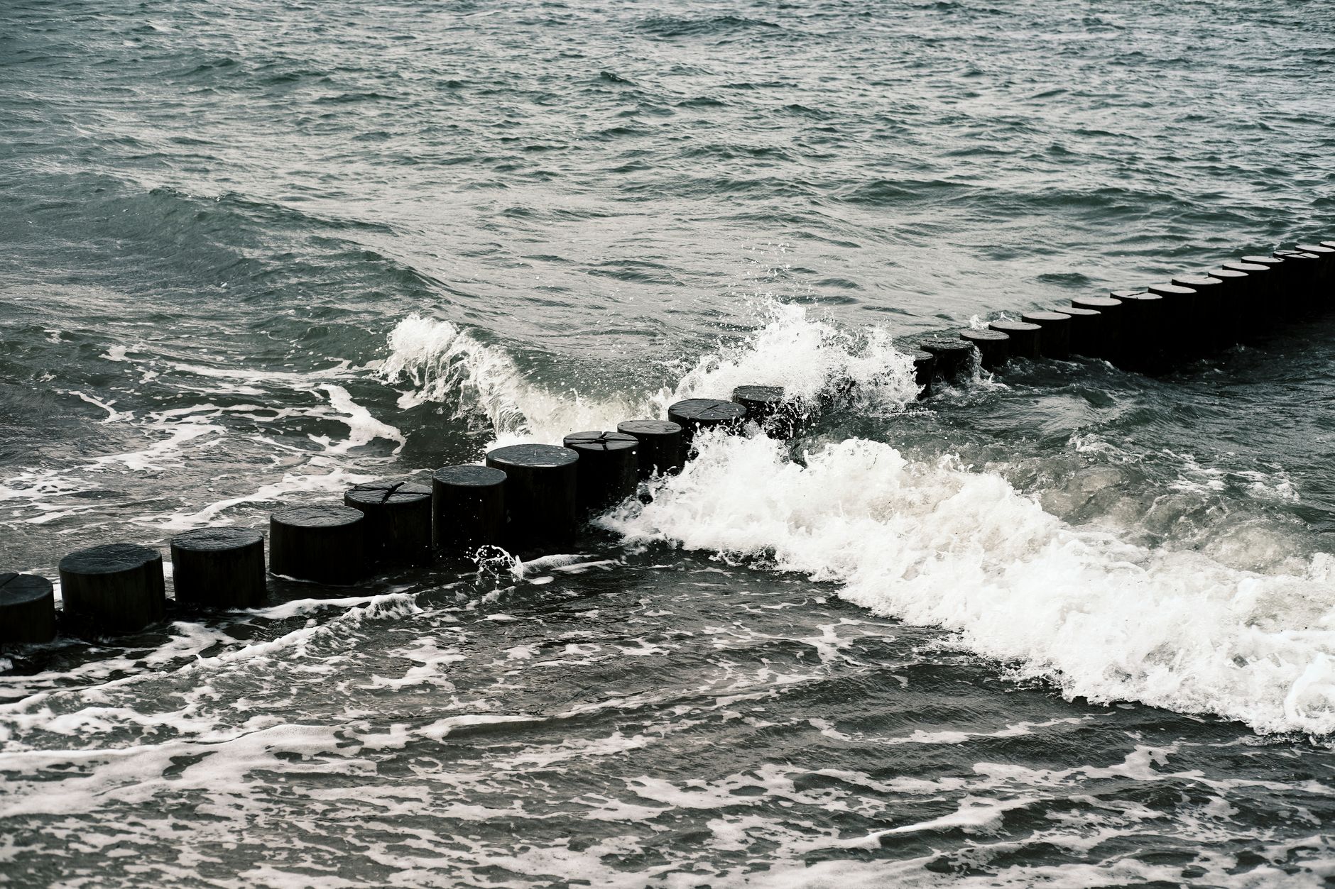 Dynamic waves crash against a wooden breakwater on the Baltic Sea, showcasing marine power.
