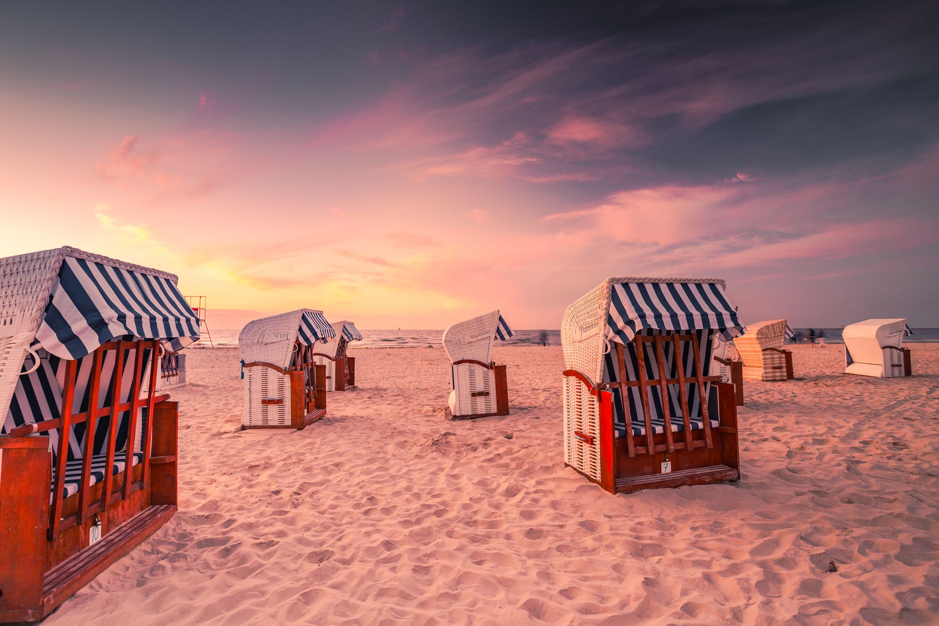 Relaxing beach scene with striped chairs and a vibrant evening sky in Świnoujście, Poland.