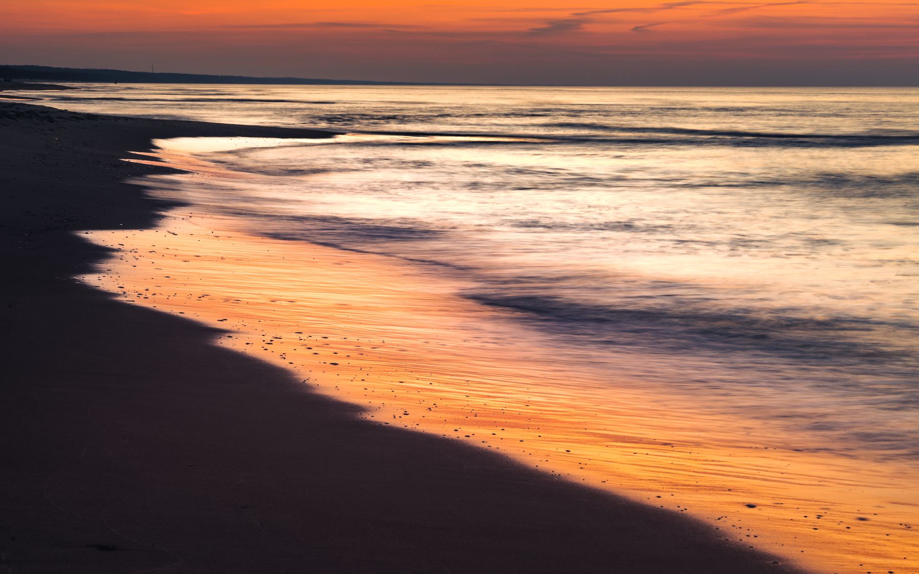Tranquil scene of waves gently washing ashore under a vibrant sunset at a beach in Poland.