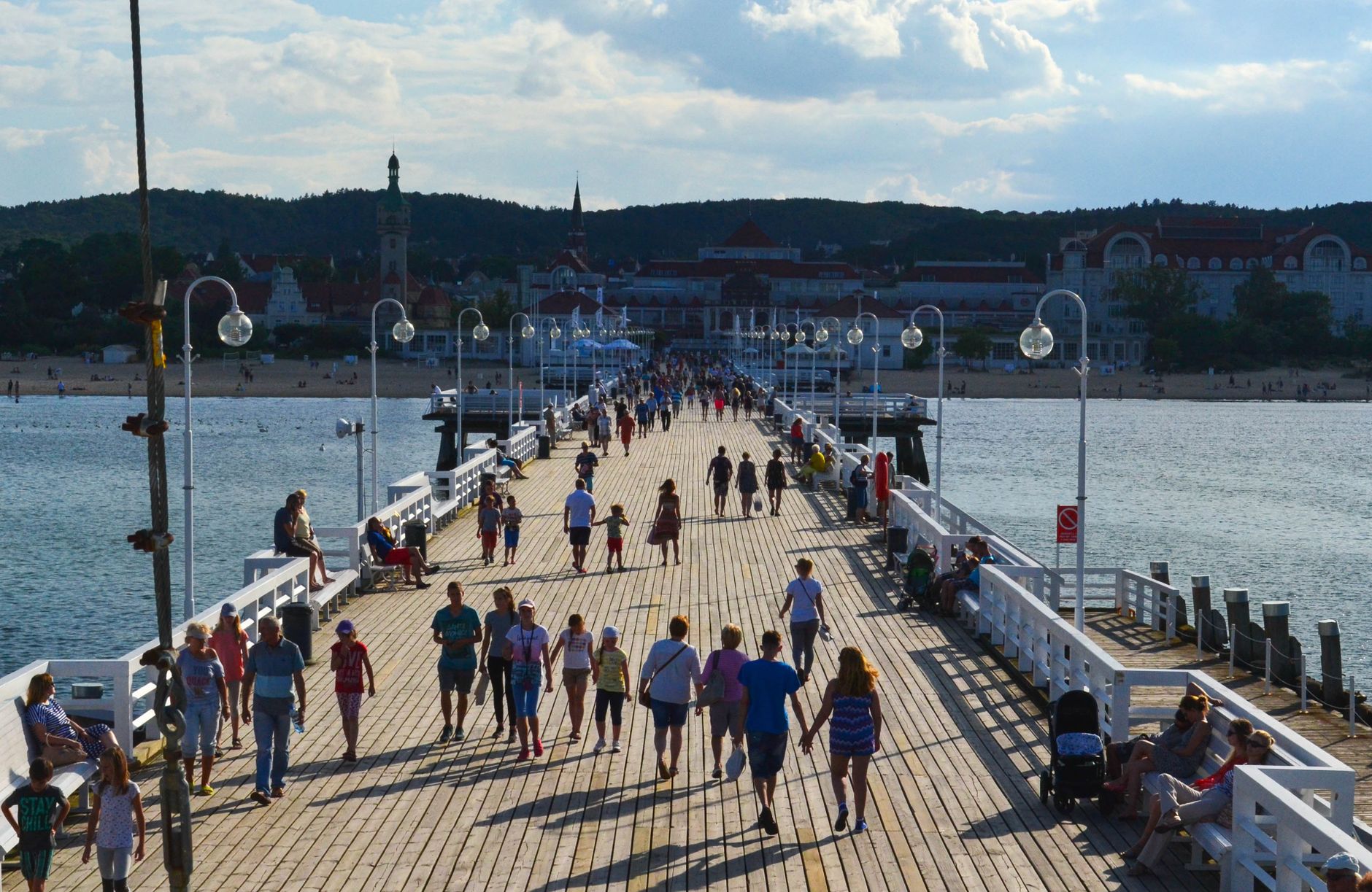 Tourists stroll along the bustling wooden pier in Gdańsk, Poland, on a sunny day.