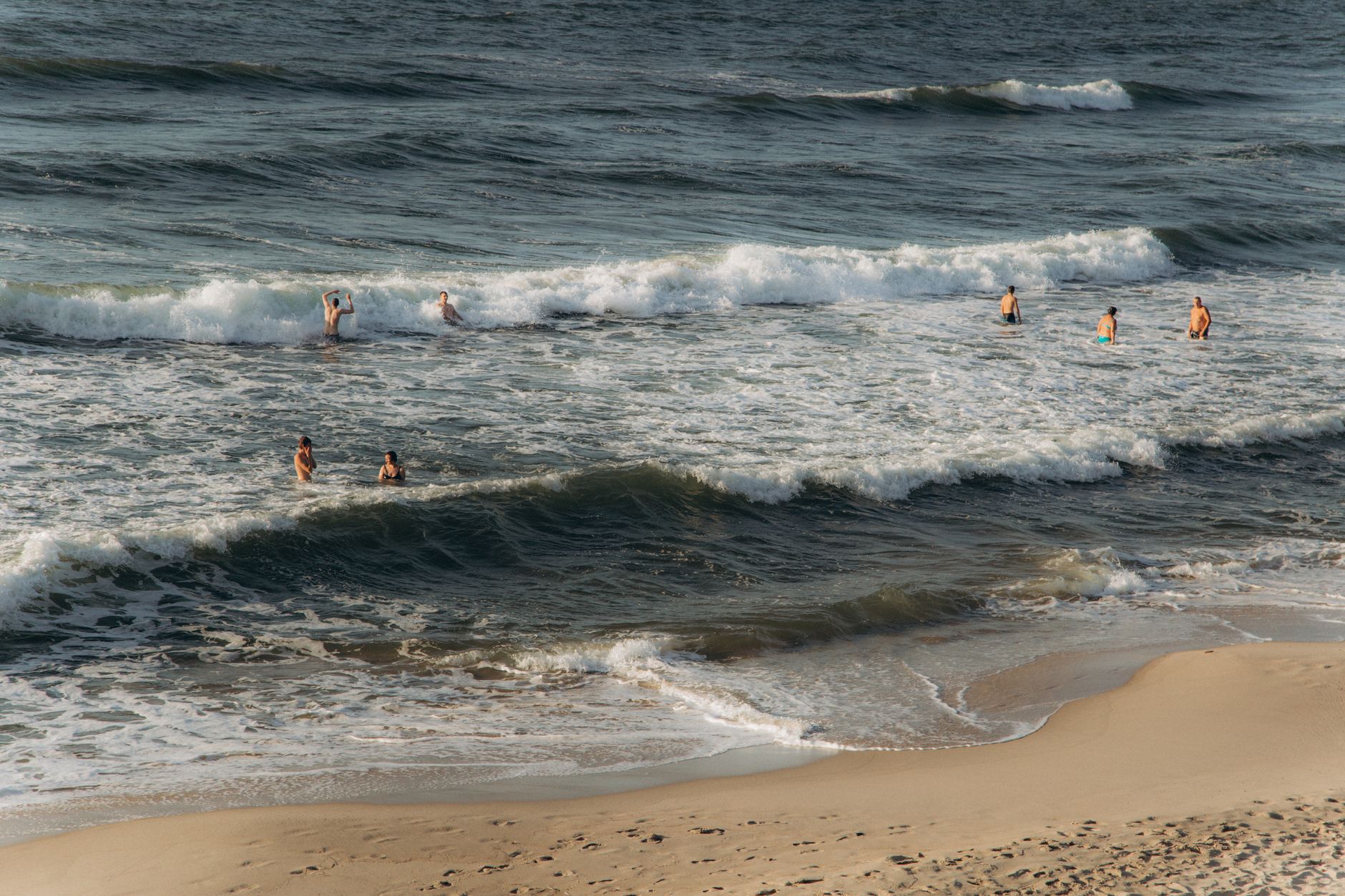 Group enjoying swimming in ocean waves at a sunny beach on a summer day.