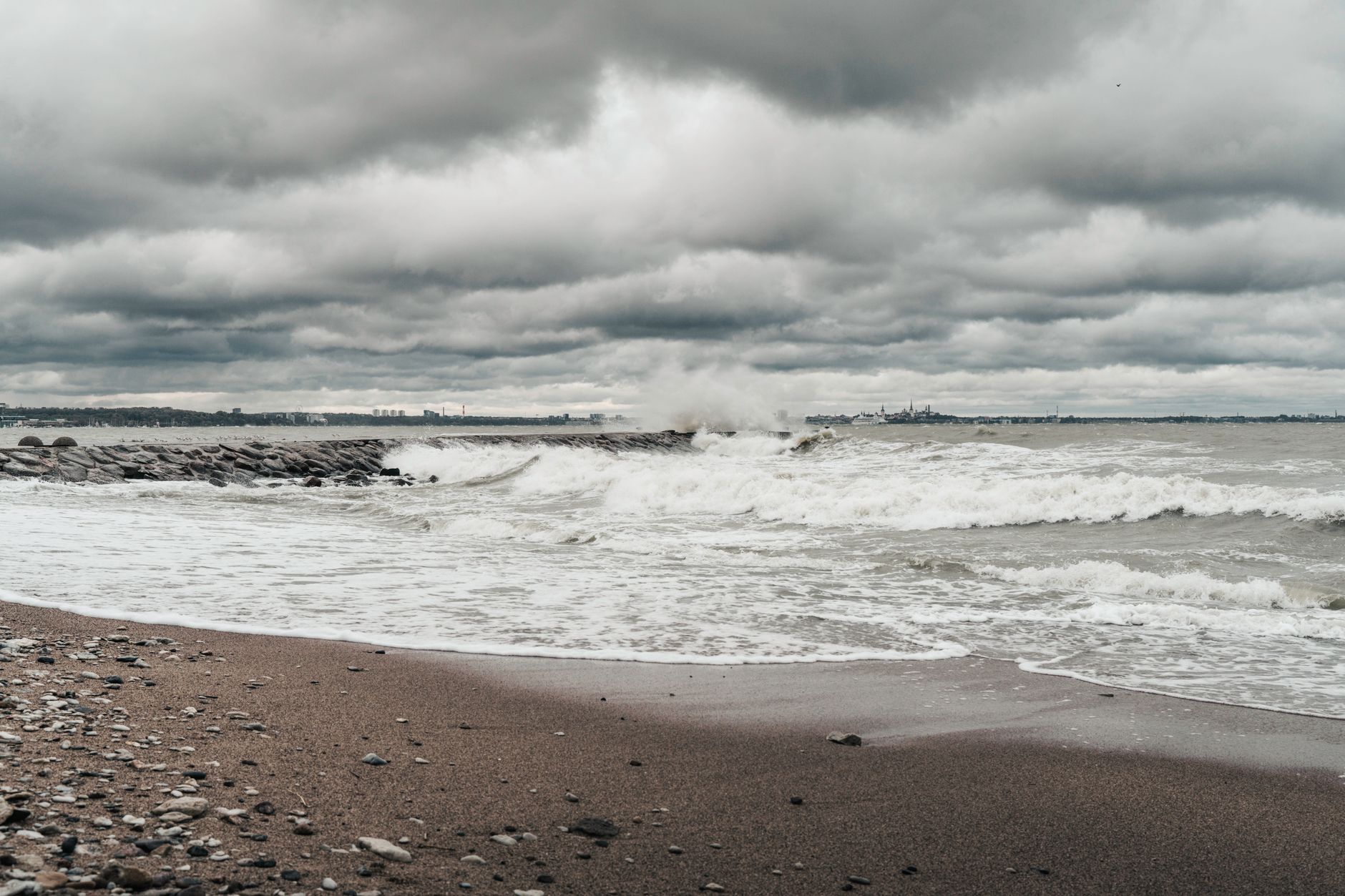 A moody, dramatic view of stormy waves crashing on an Estonian beach under overcast skies.