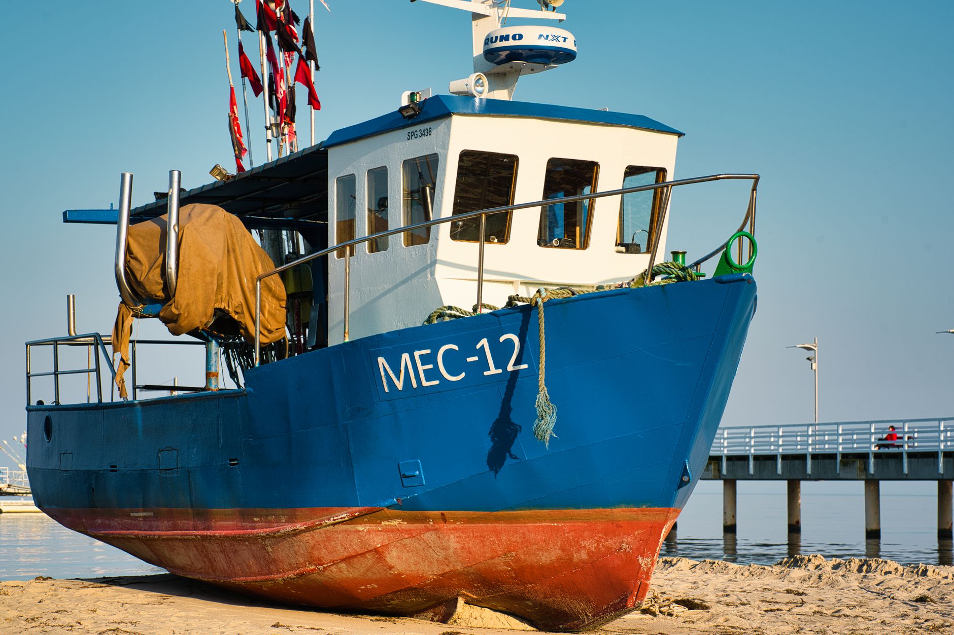 Colorful fishing boat MEC-12 resting on the sandy shore by a pier in Poland.