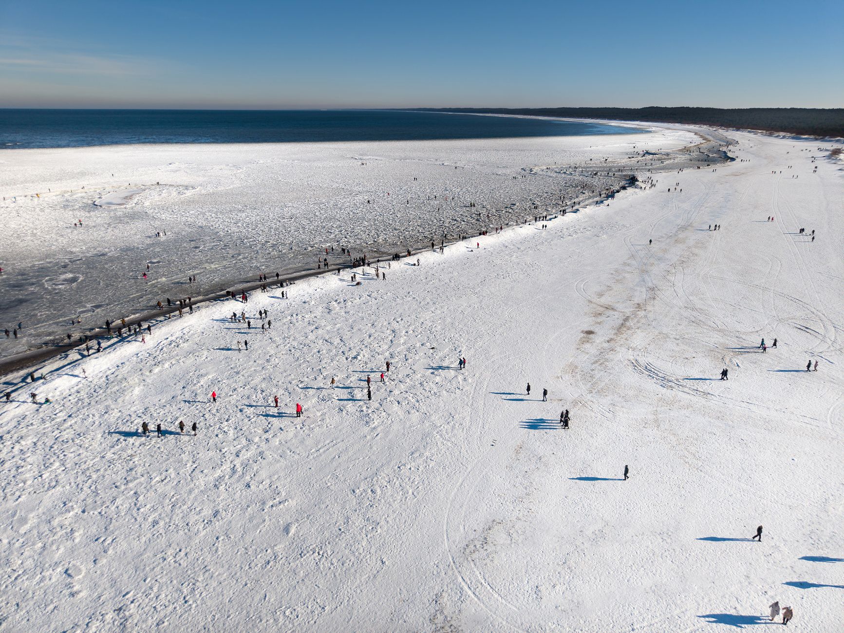 A stunning aerial view of the frozen Baltic coastline with people walking on the snowy beach.