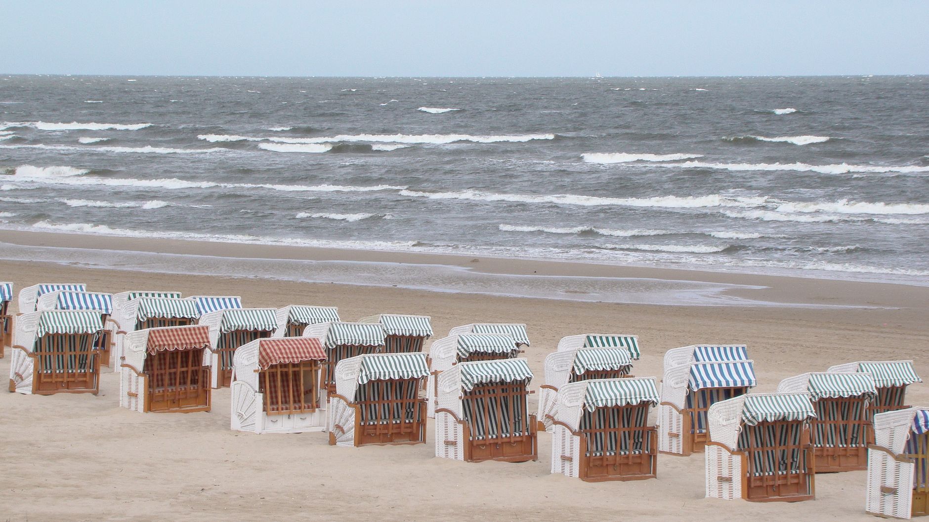 Calm beach scene with lined beach chairs facing the sea under a clear sky.