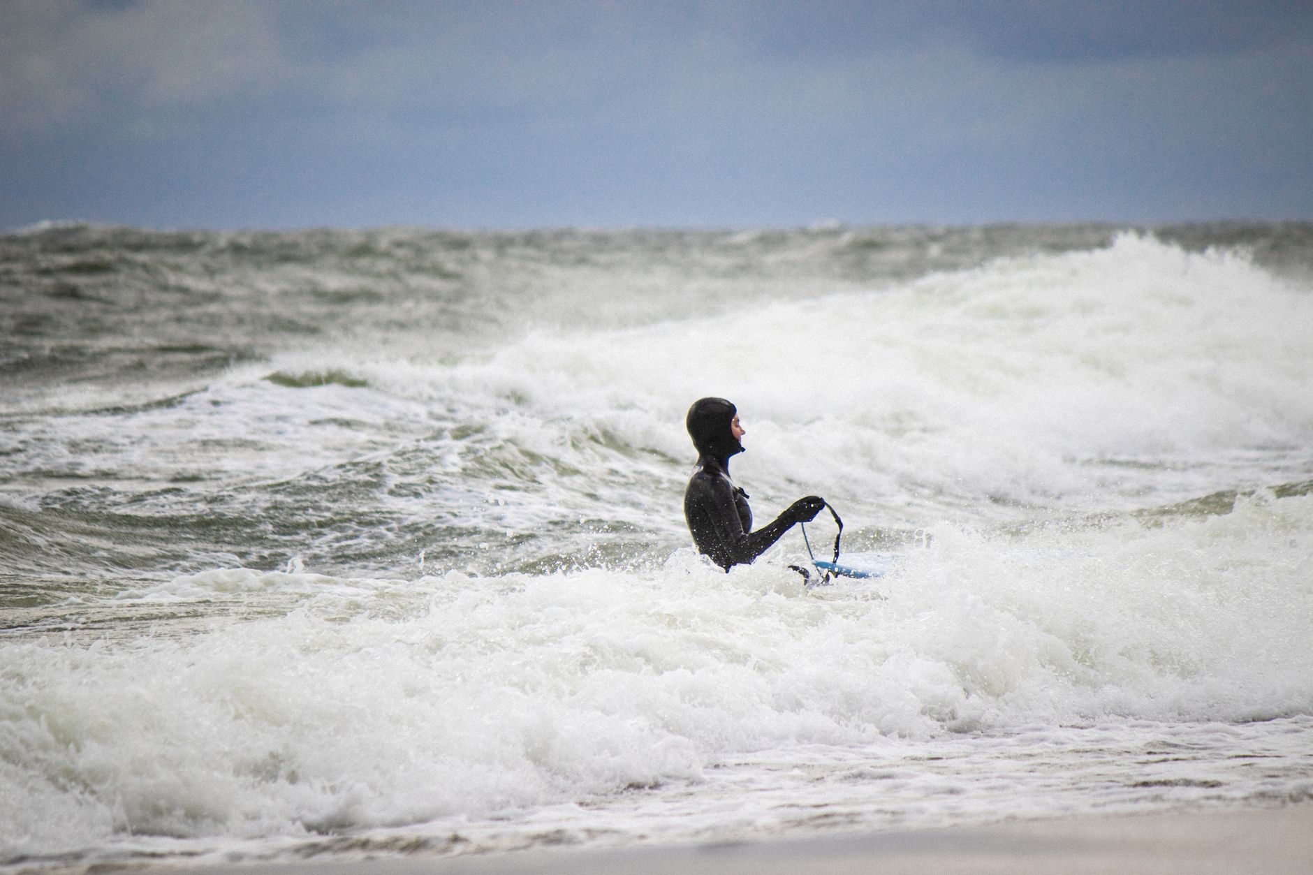 Woman surfer faces powerful Baltic Sea waves at Jastrzębia Góra, Poland, highlighting strength and determination.