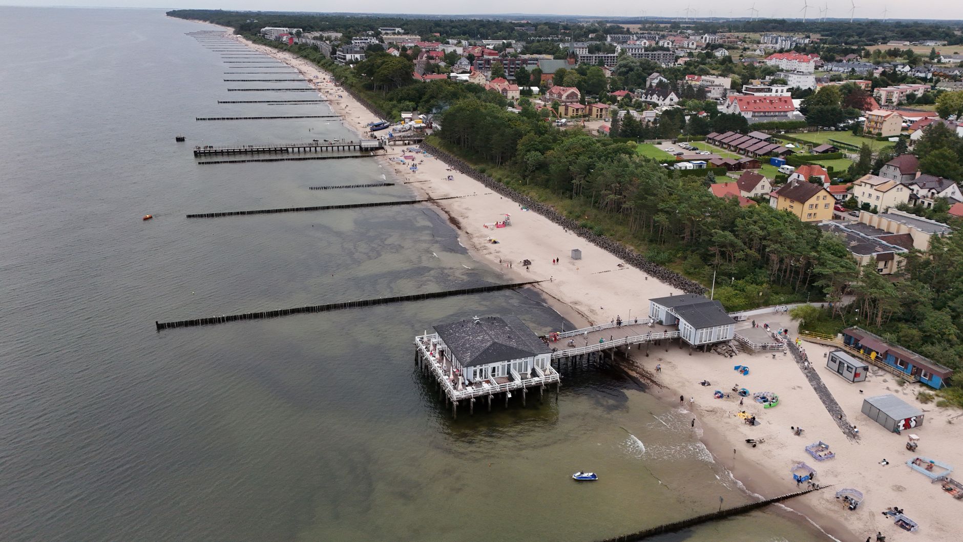 Aerial shot of a coastal town with beach, pier, and waterfront buildings.