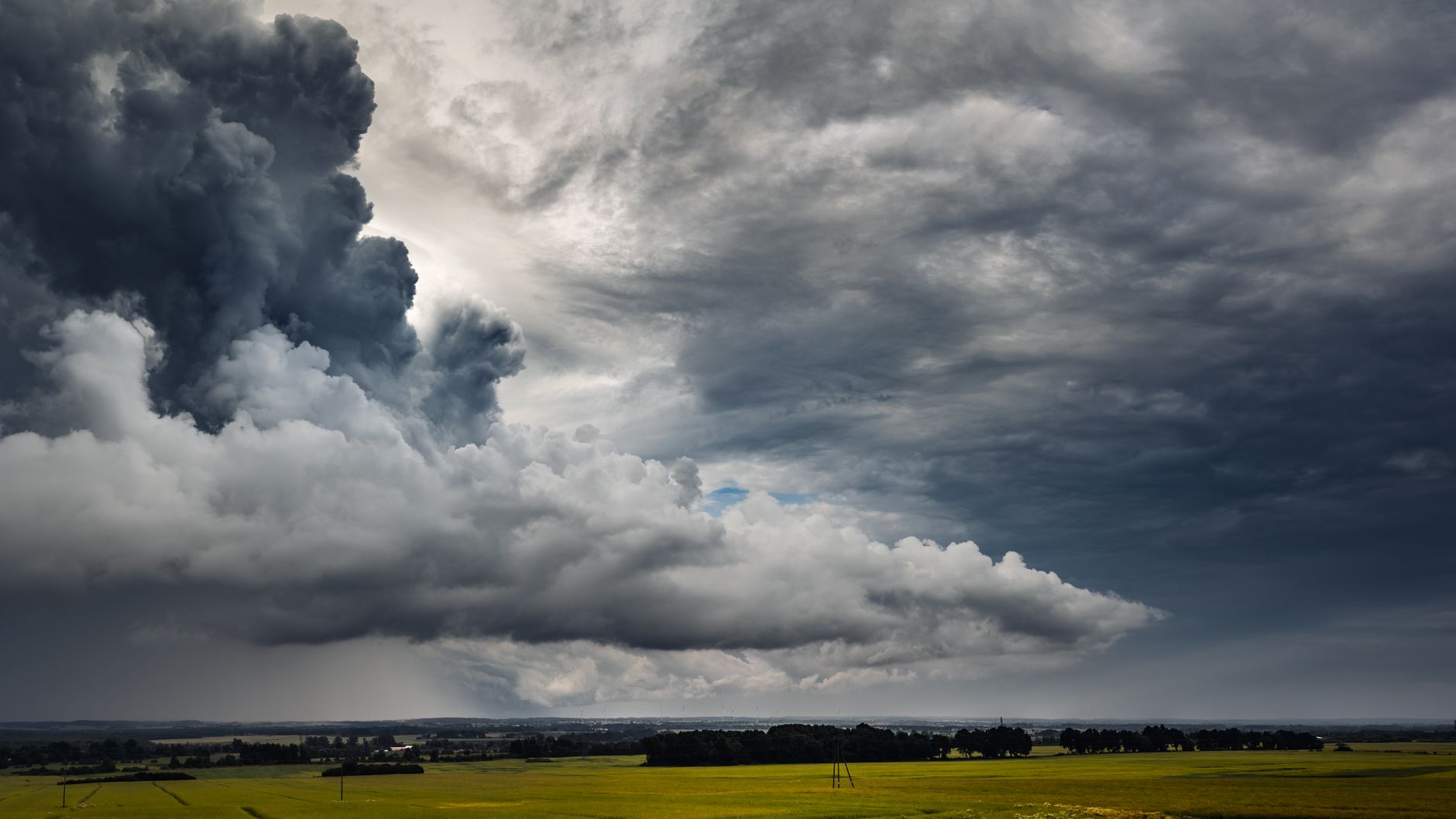 Dark storm clouds loom over the green fields of Poland, capturing nature's power.