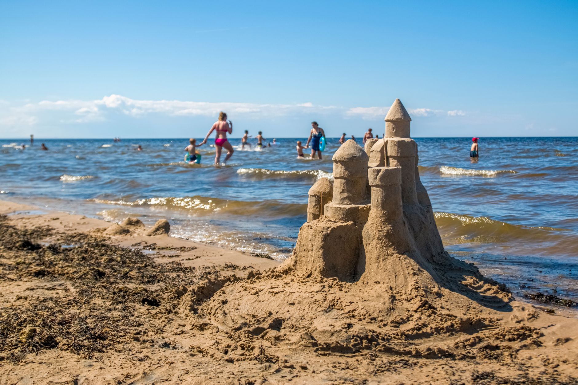 Big sandcastle built on sandy shore washed by calm waving sea on public crowded beach