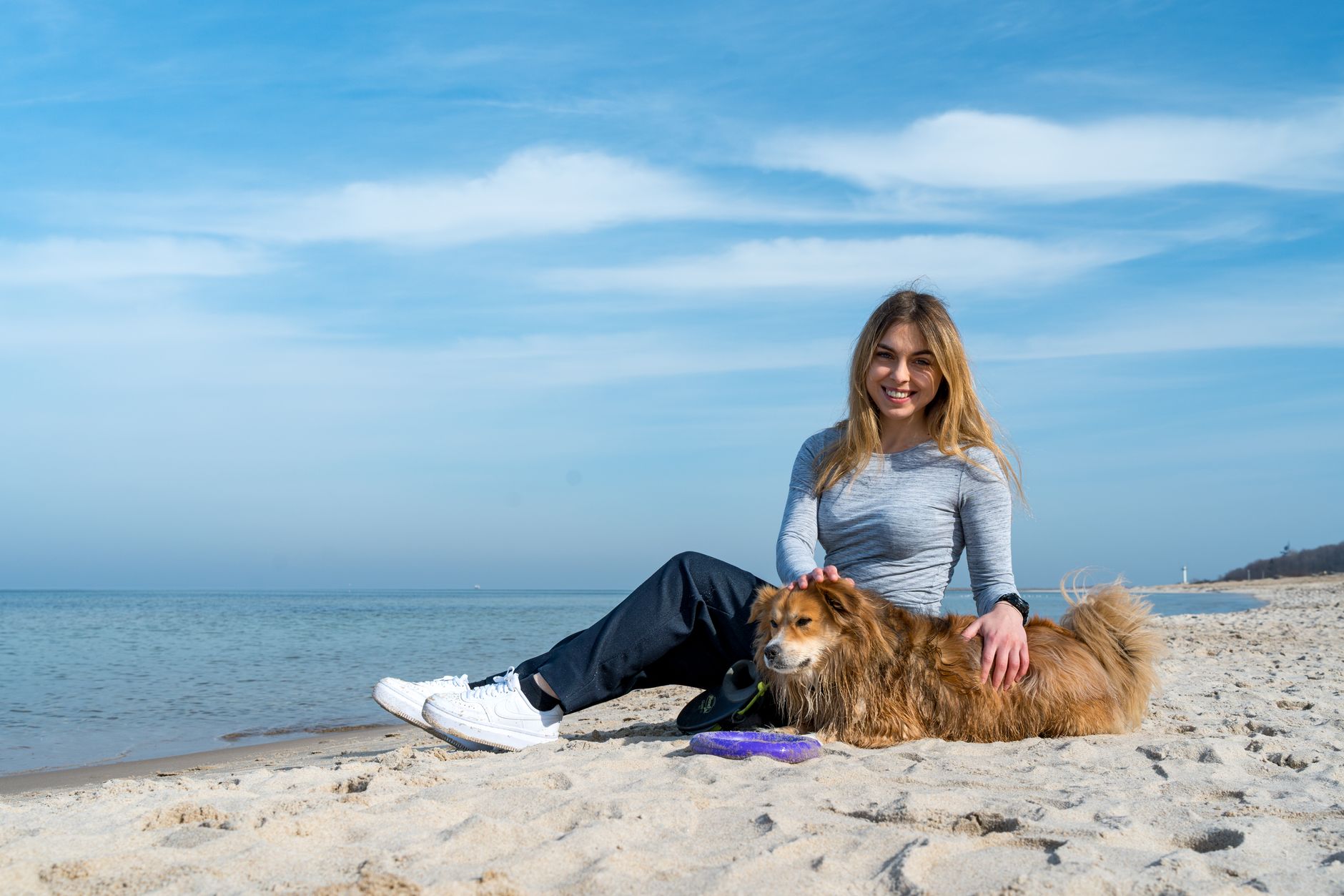 Woman enjoying a sunny day on Kołobrzeg beach with her dog, capturing the essence of leisure and companionship.