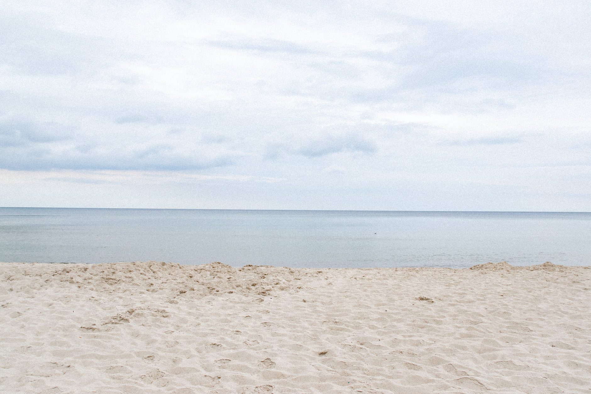 Serene view of Świętouść Beach, Poland, showcasing a sandy shore and calm sea under a cloudy sky.