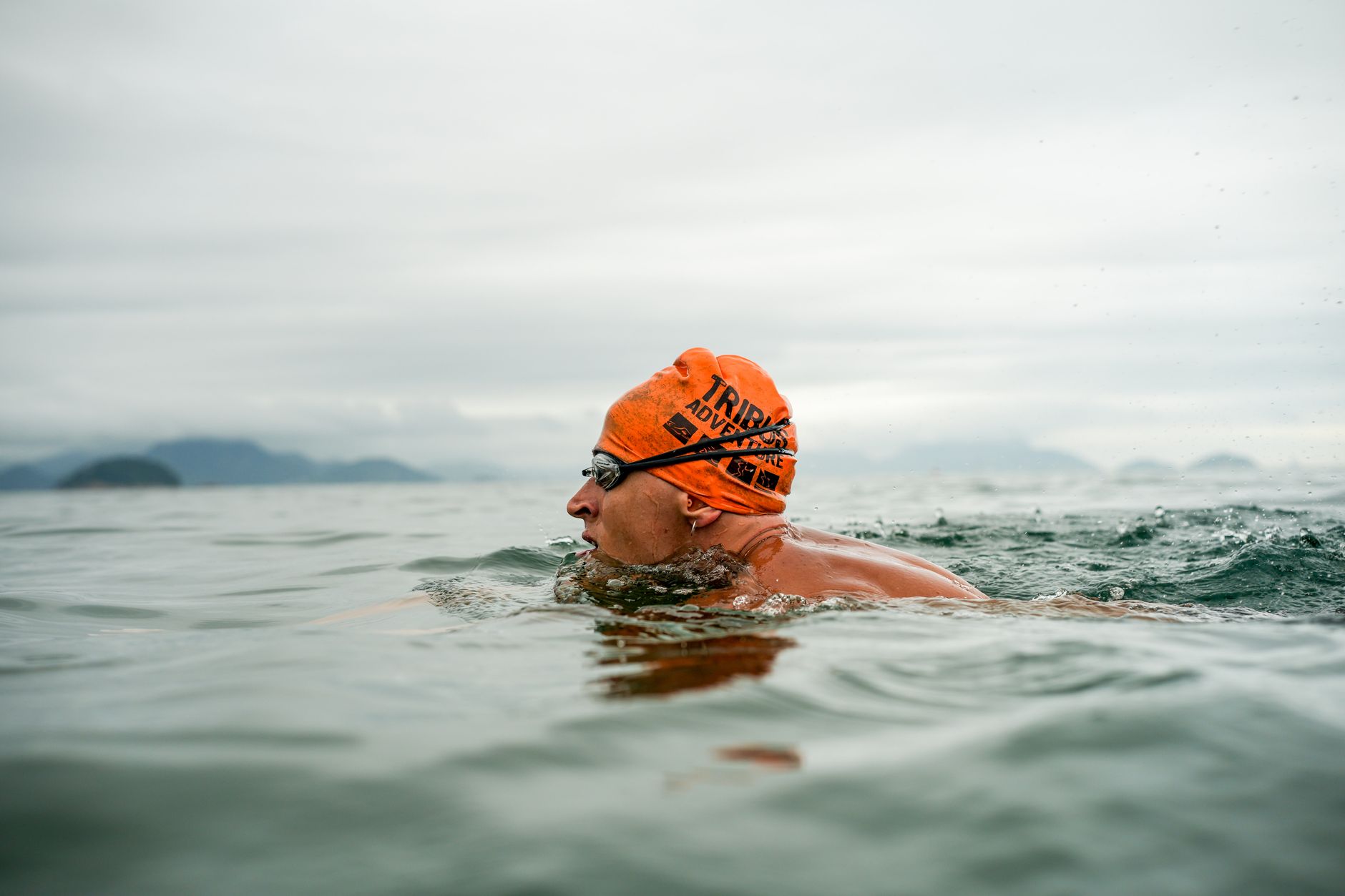 Adult male swimmer in open water wearing an orange swim cap and goggles, swimming in the sea.