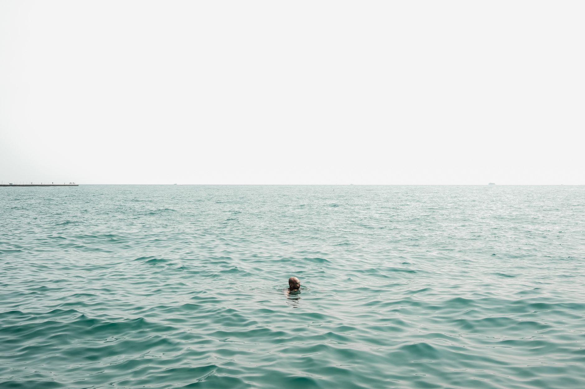 A lone swimmer in a vast expanse of open water under an overcast sky.