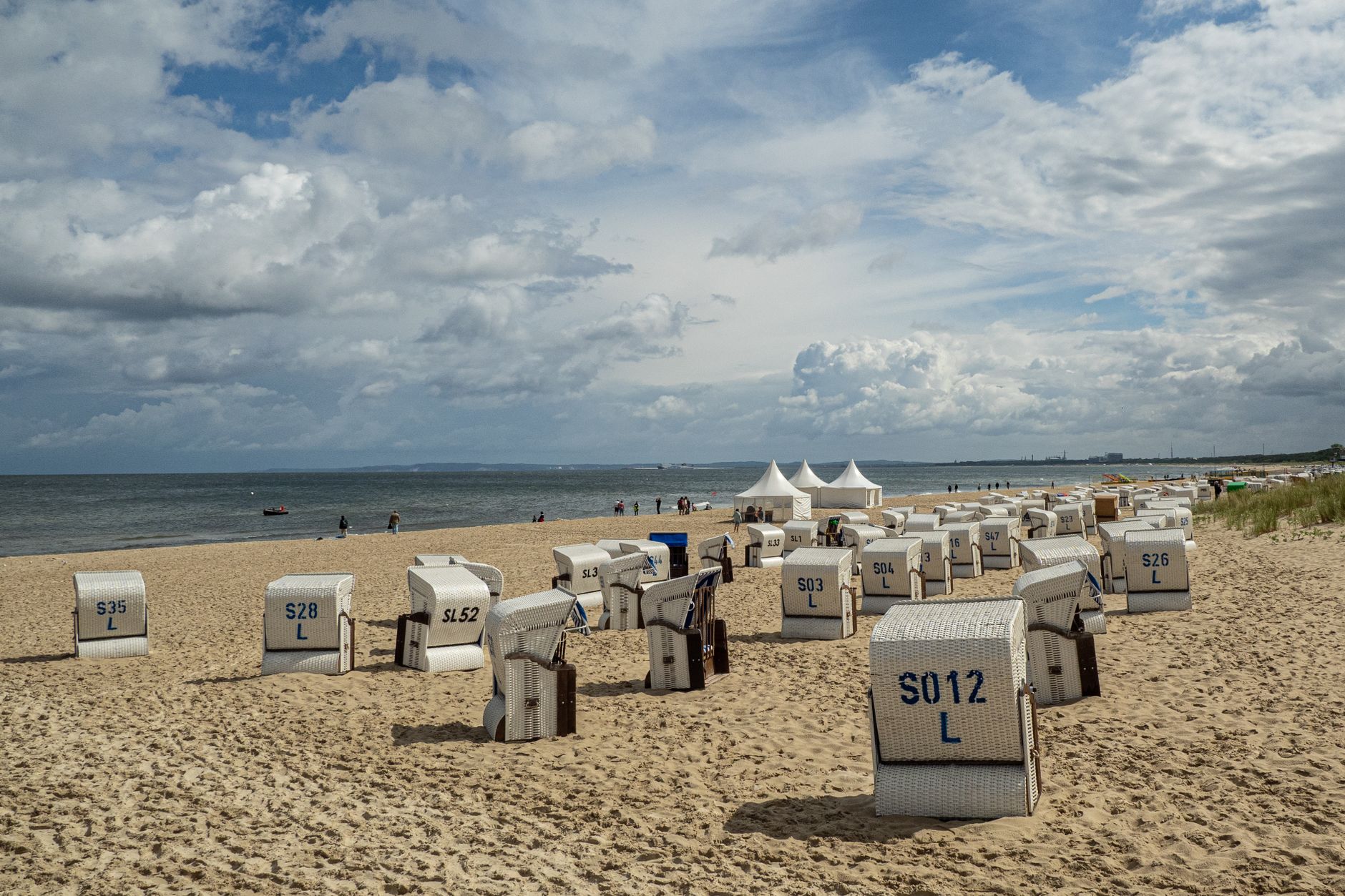 Serene beach scene with wicker chairs facing the sea under partly cloudy skies.