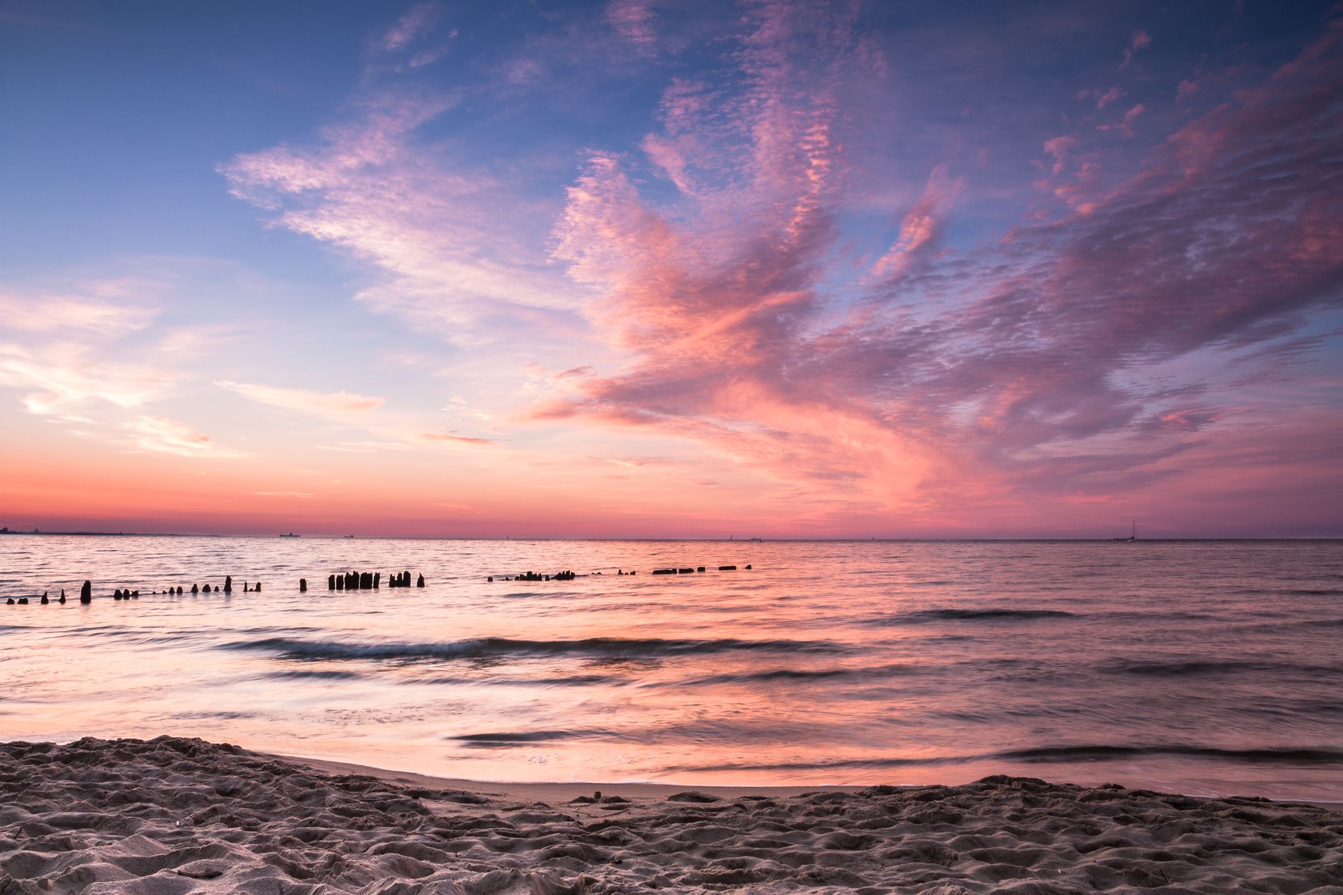 Capture the serene beauty of a Gdańsk beach at sunset with vibrant pink and orange skies.