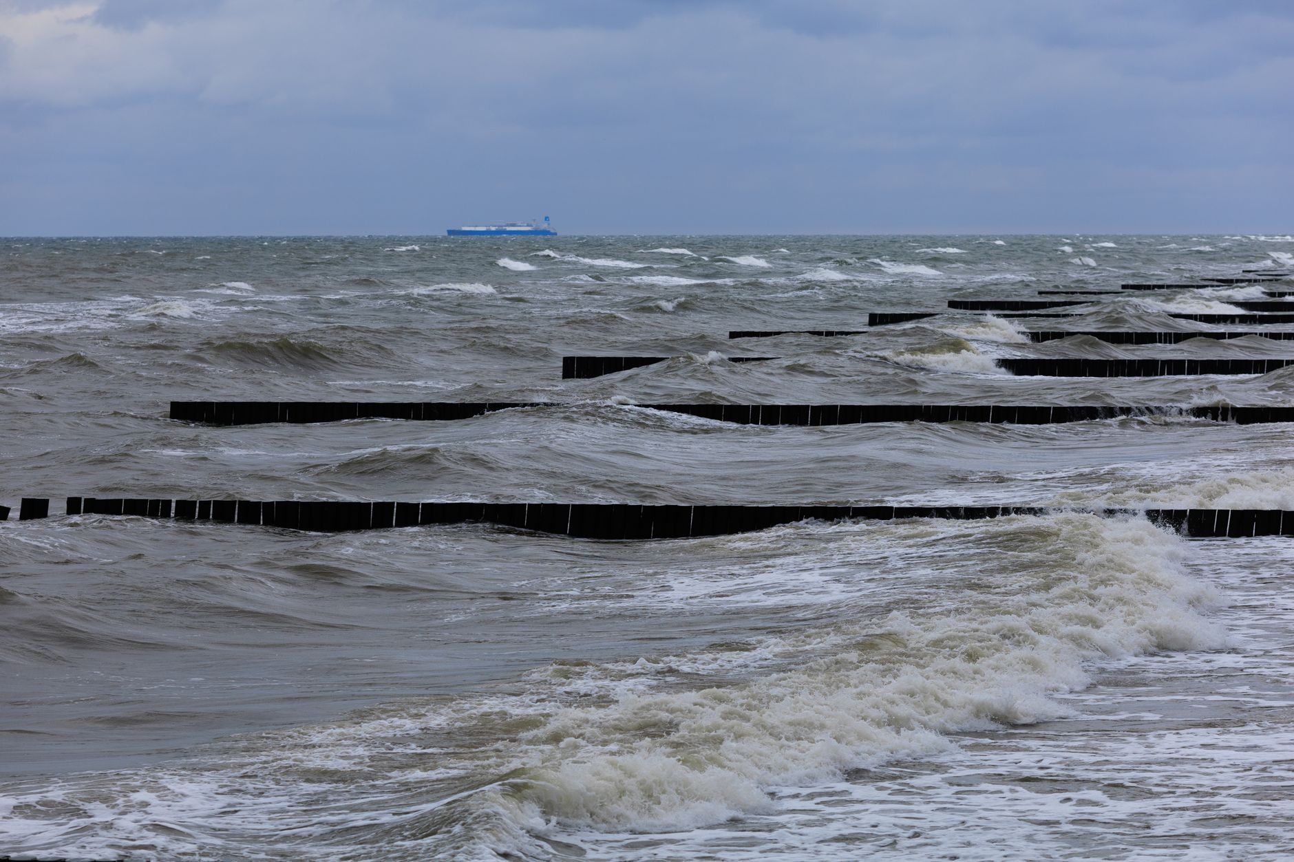 Wild ocean waves crashing against the breakwater with a ship on the horizon.