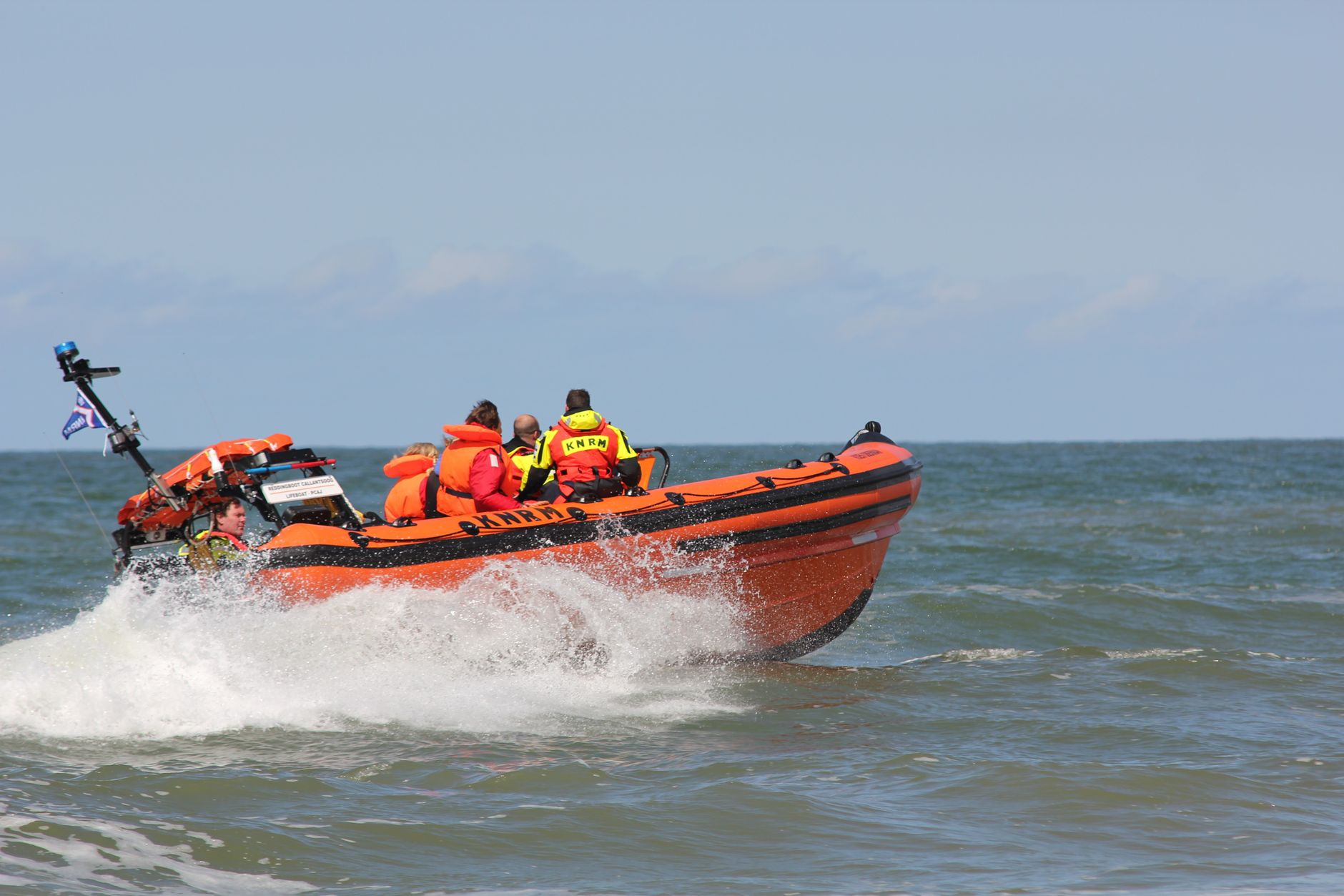 Emergency rescue team navigating rough seas in an orange motorboat during daytime patrol.