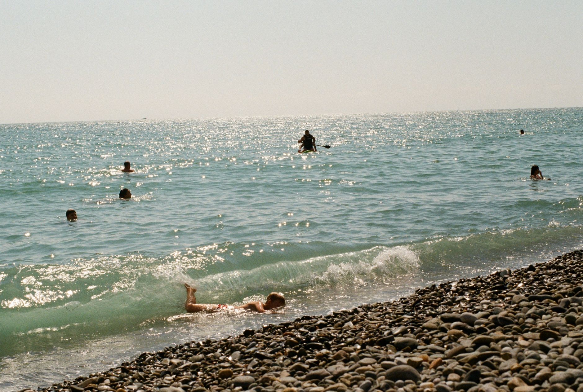 People enjoying a sunny day swimming in the ocean at a pebble beach.