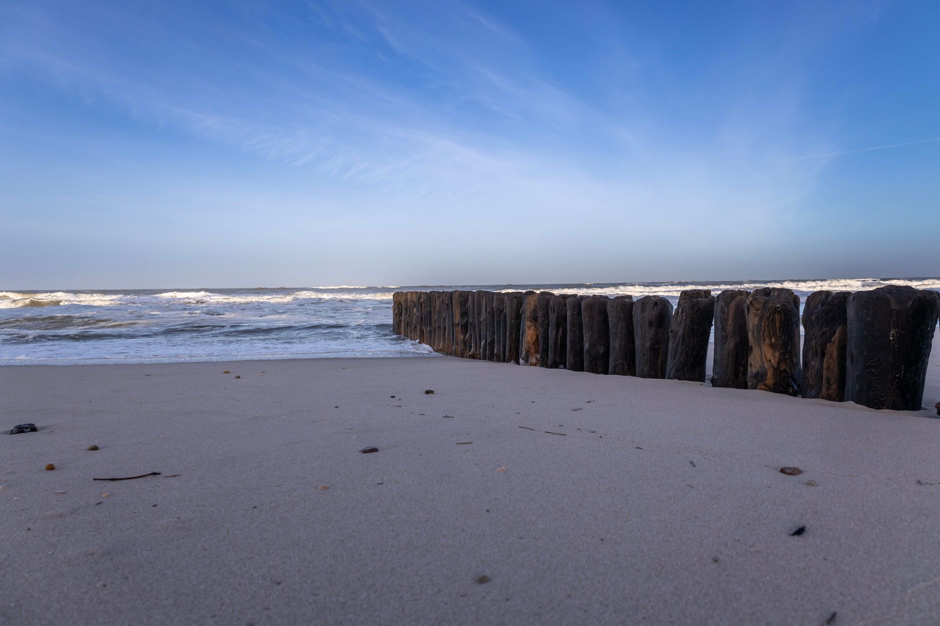 Calming view of a sandy beach with wooden groynes, waves, and blue sky at Sylt, Germany.