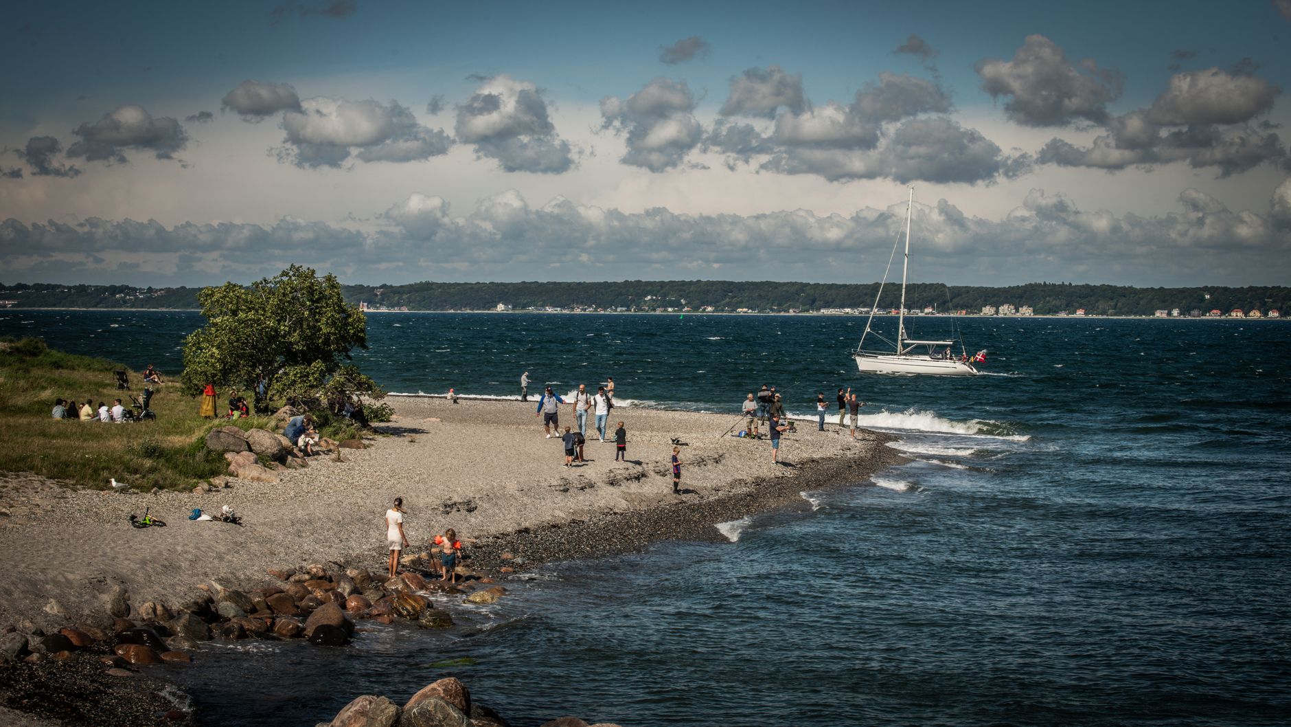 Relaxed beach scene with people enjoying summer at Helsingør, Denmark. Yacht sailing in the Baltic Sea.