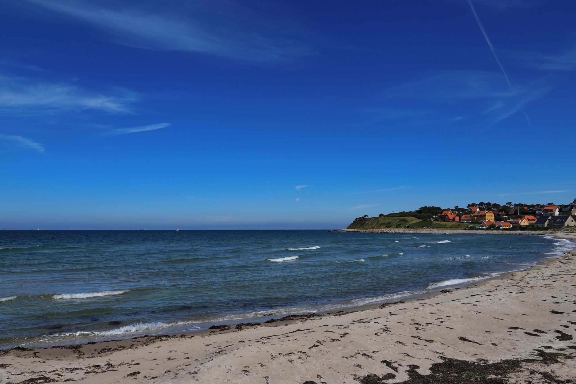 Beautiful view of a sandy beach in Hundested, Denmark, with colorful houses by the sea.