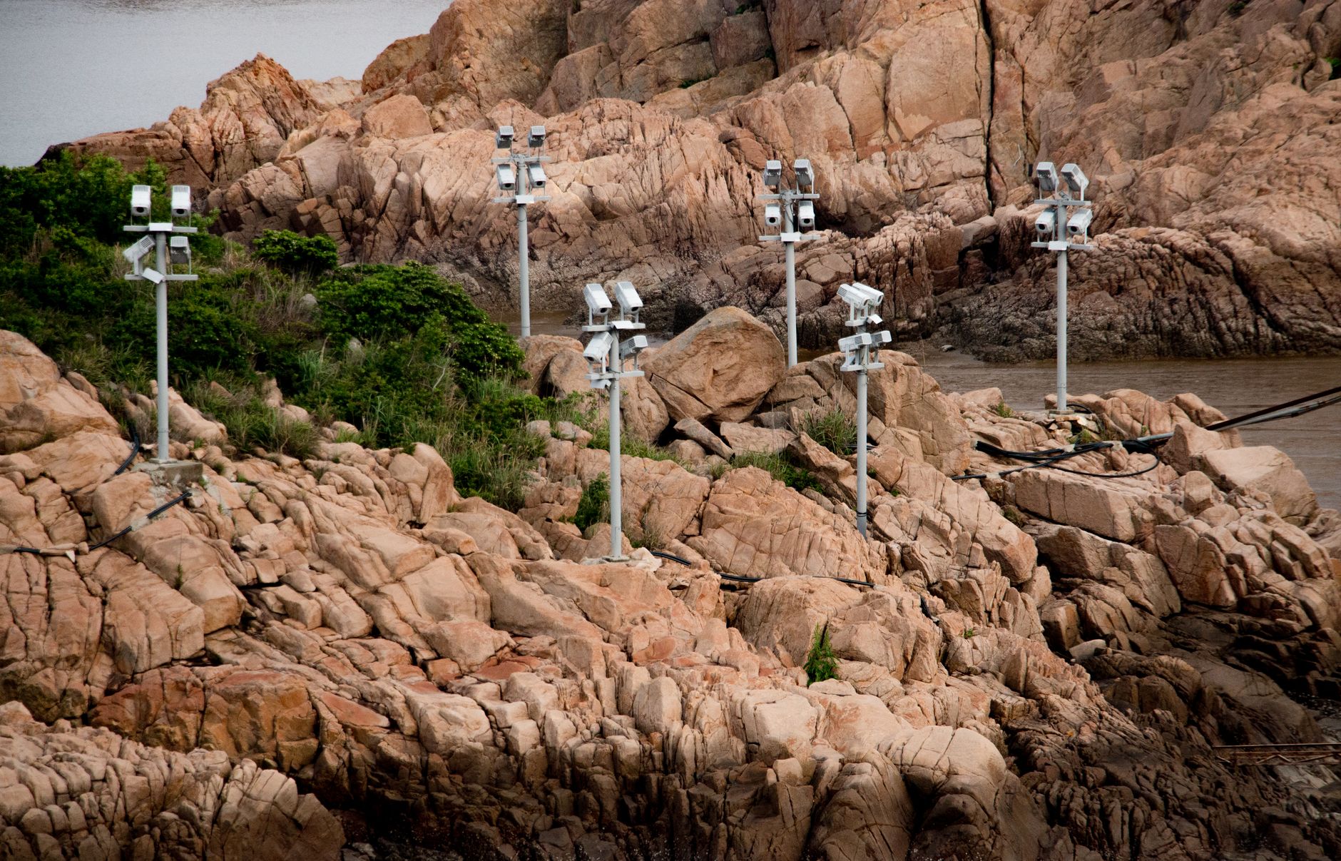 Multiple surveillance cameras monitor a rocky coastline with surrounding vegetation.