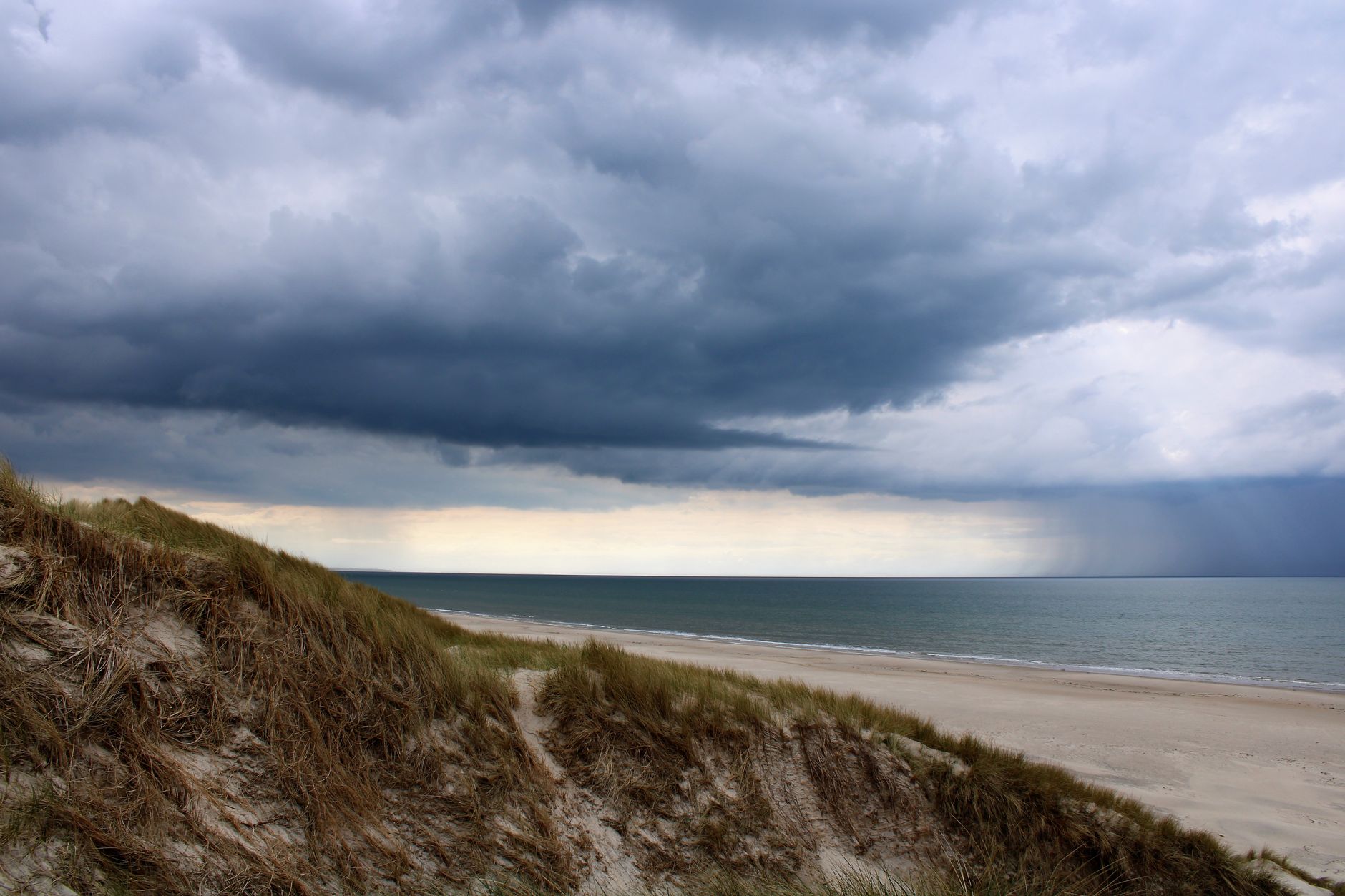 Stormy clouds gather over the sandy shores of Lønstrup Beach, creating a moody seascape in Denmark.