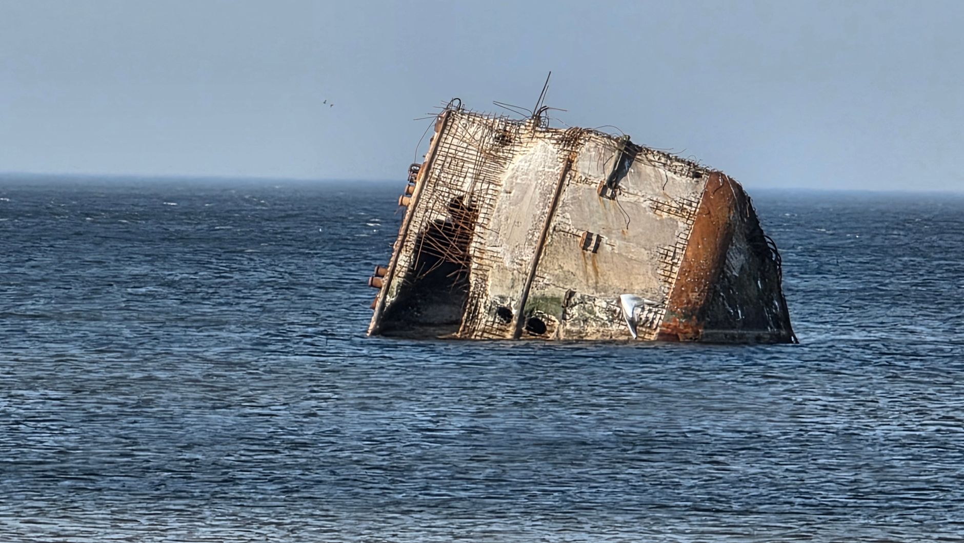 A haunting image of a corroded structure emerging from the Baltic Sea waters under a blue sky.