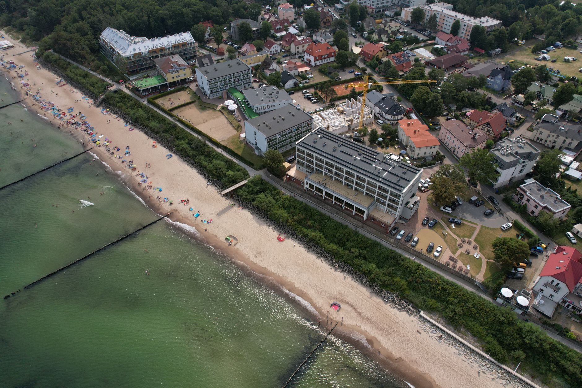Aerial shot capturing a town along a sandy beach by the ocean, featuring buildings and greenery.