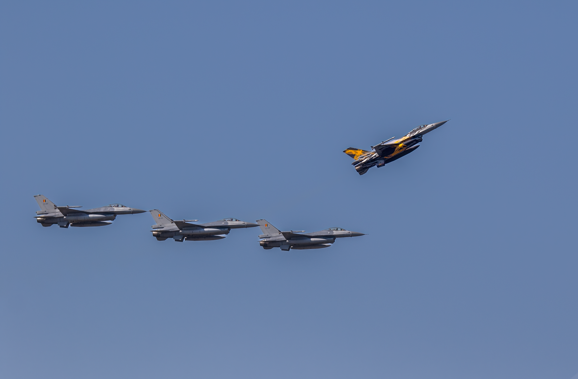 Aerial view of F-16 fighter jets flying in formation against a clear blue sky.