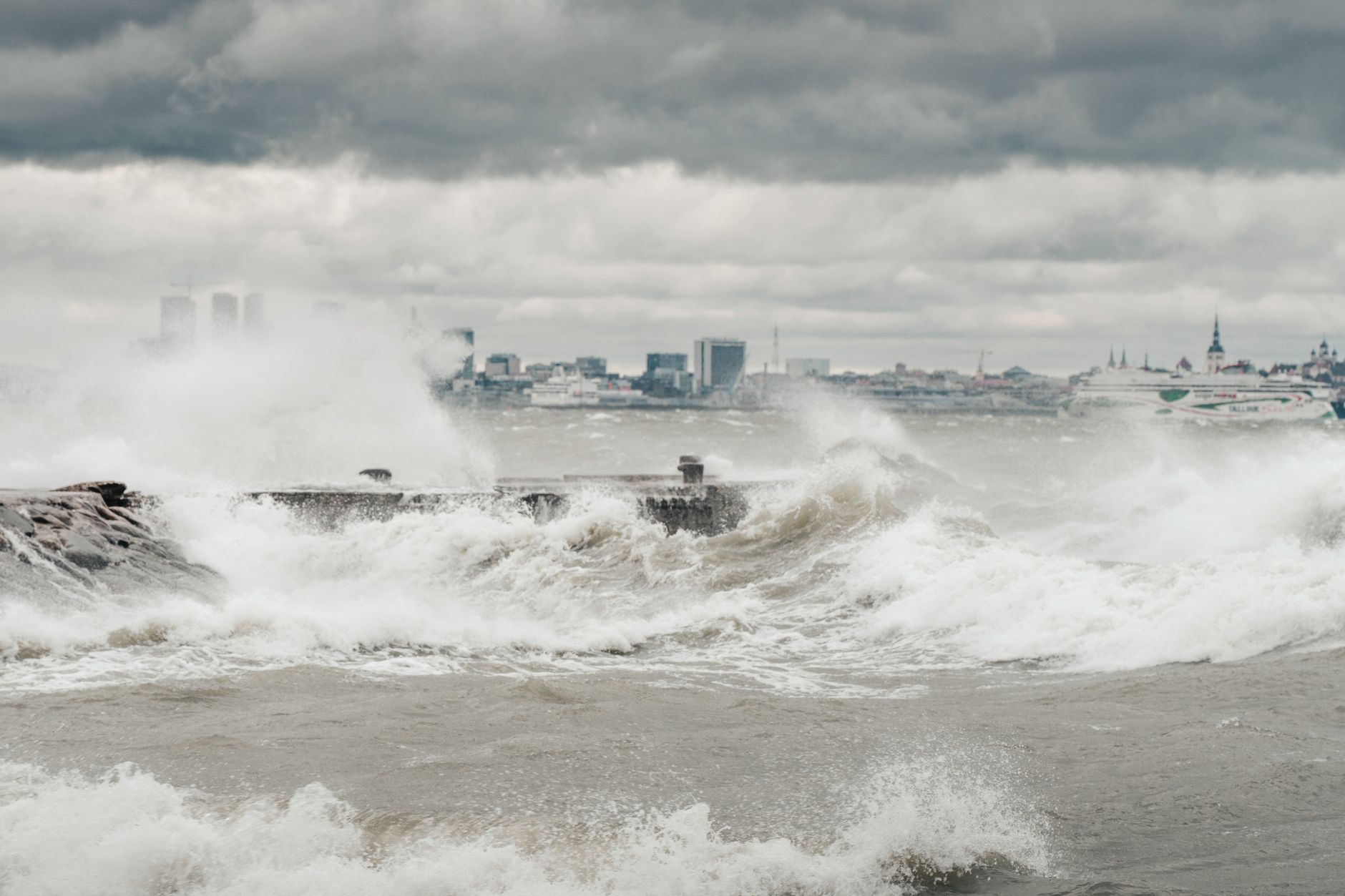 Powerful waves crash against the Tallinn coastline under stormy skies, creating a dramatic seascape.