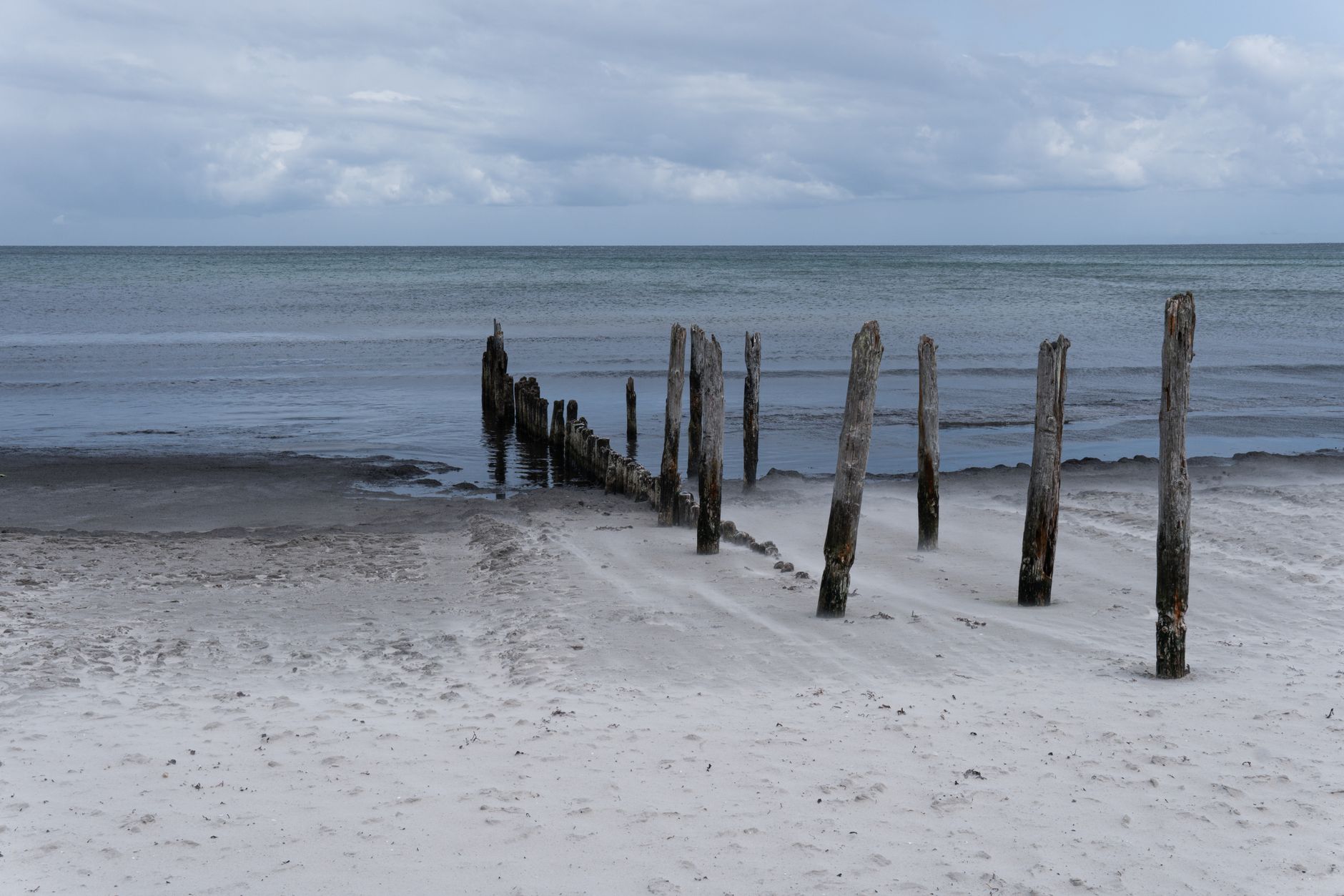 A tranquil beach with old wooden posts by the sea under a cloudy sky.