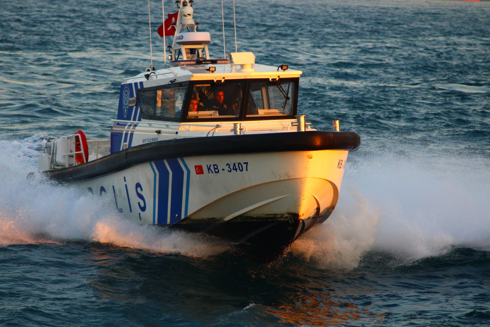 Dynamic capture of a Turkish police boat slicing through ocean waves at high speed, flag in view.