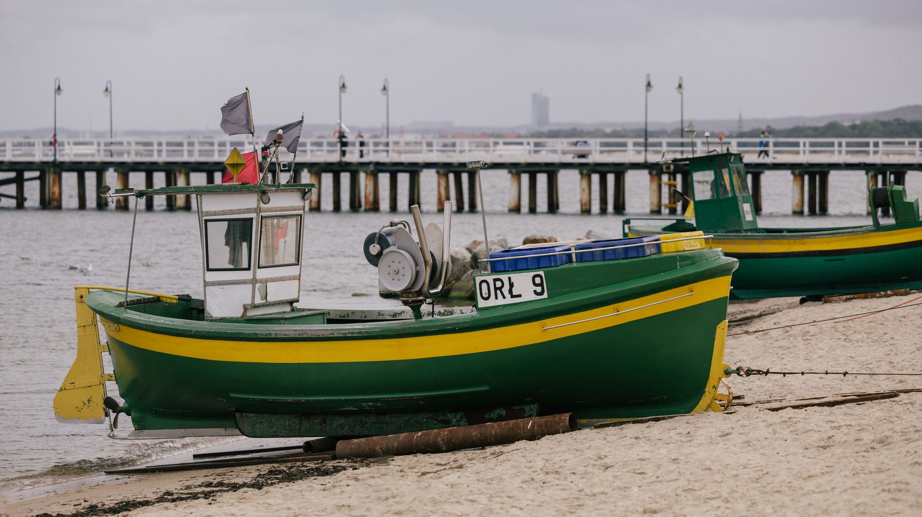 Vibrant green and yellow fishing boats on a beach near a pier, with an overcast sky.