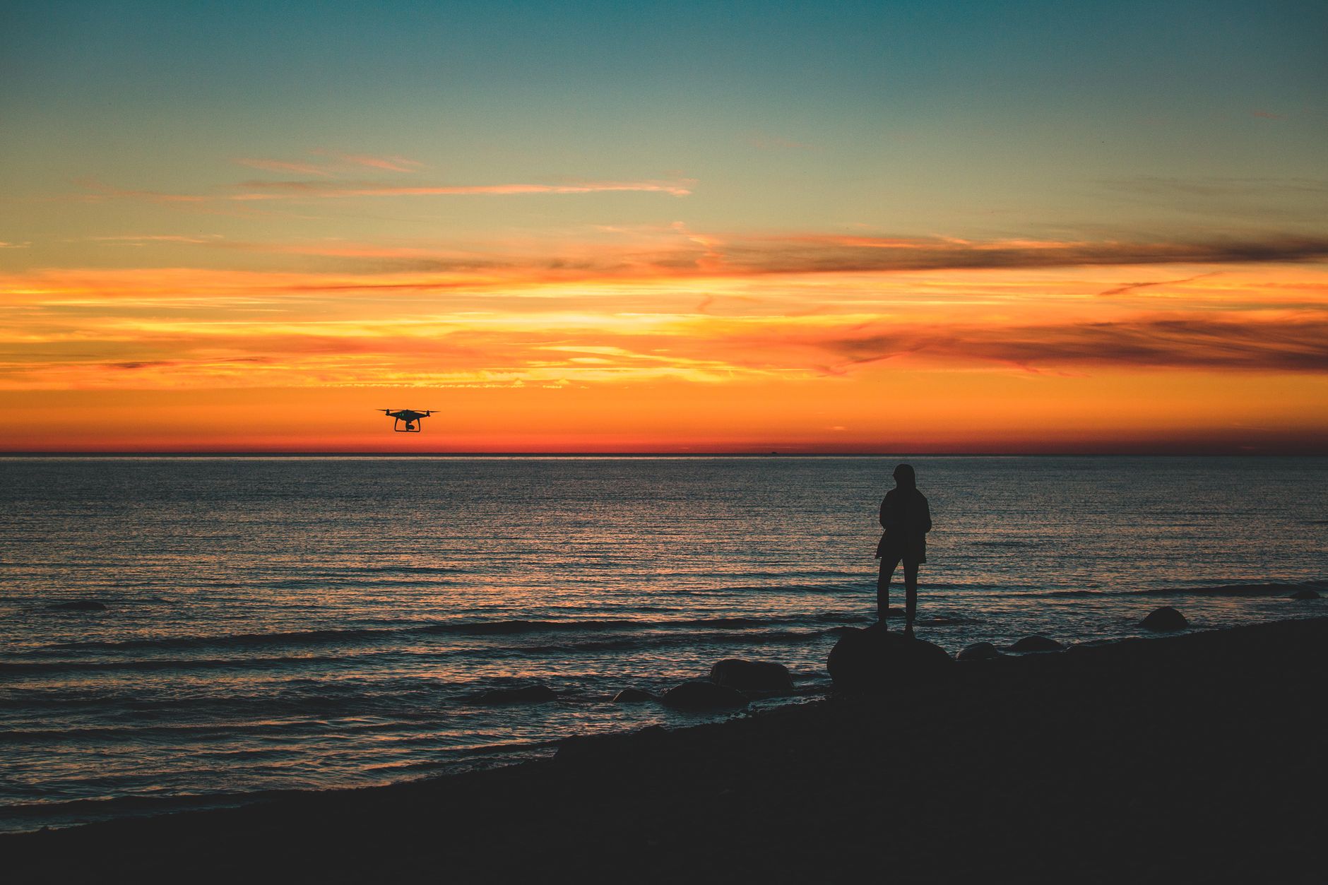 Captivating sunset with a drone flying over the Baltic Sea, featuring a silhouetted person on the shore.