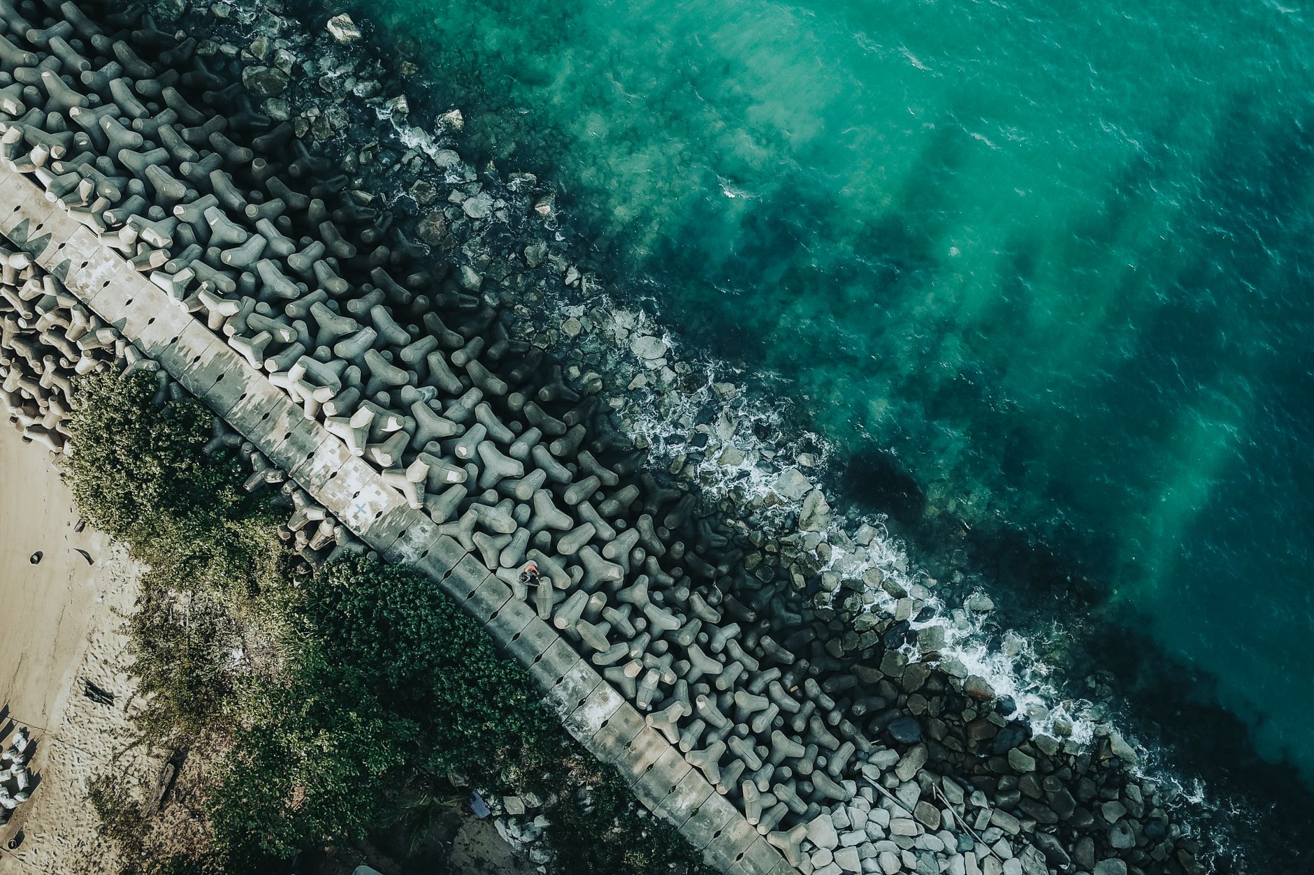 Aerial view of a concrete breakwater along a pristine coastline meeting blue ocean waves.