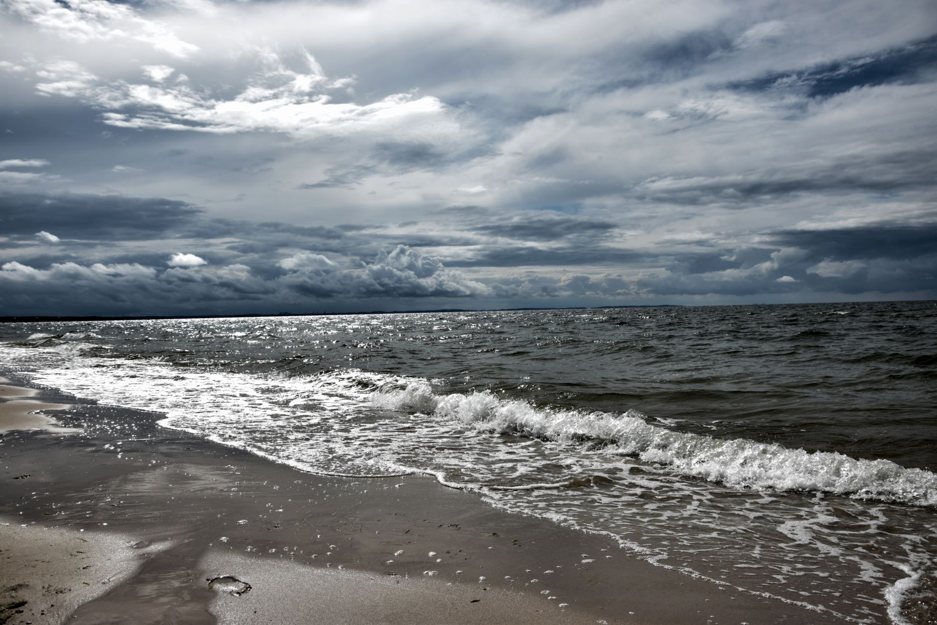 A dramatic view of a sandy beach with stormy clouds and waves crashing on the shore.