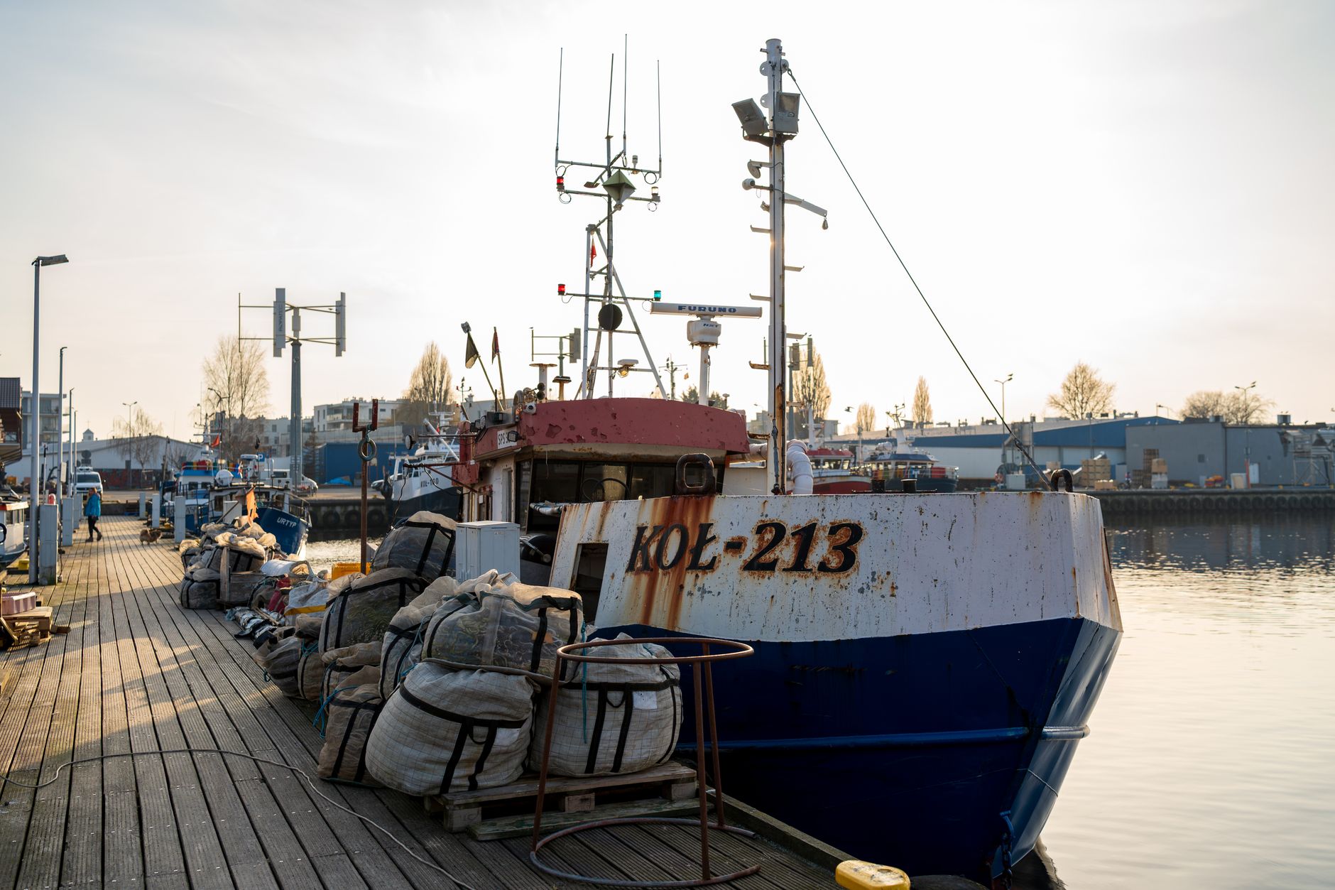 A vibrant fishing boat docked at Kołobrzeg harbor in Poland, surrounded by nets and equipment.
