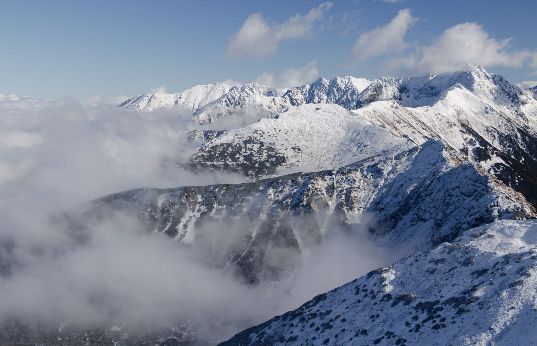 Majestic view of snow-covered Tatra Mountains in Poland with clear sky and clouds.