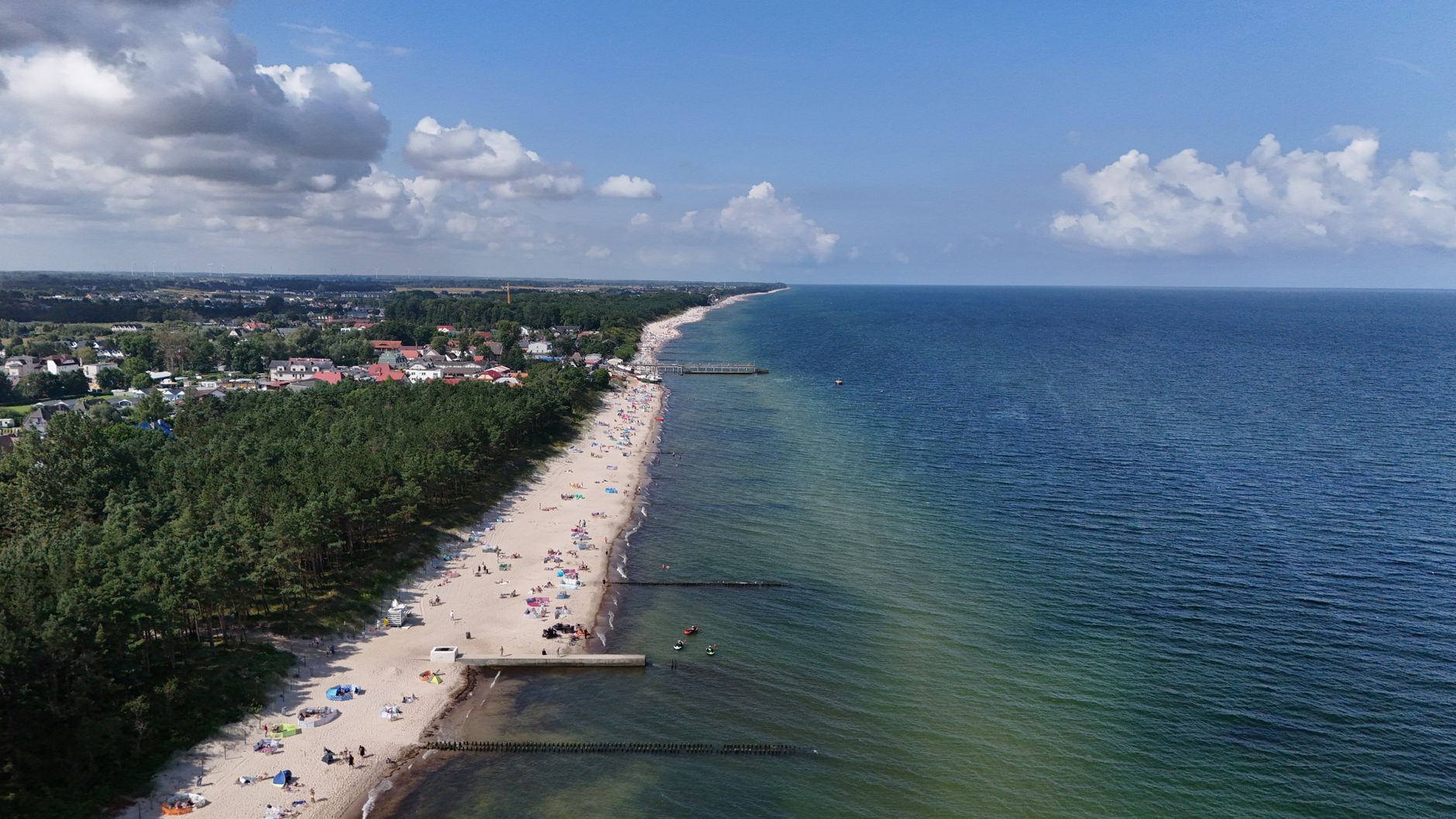 A breathtaking aerial shot of a sandy beach, vibrant ocean, and coastal town under a clear blue sky.