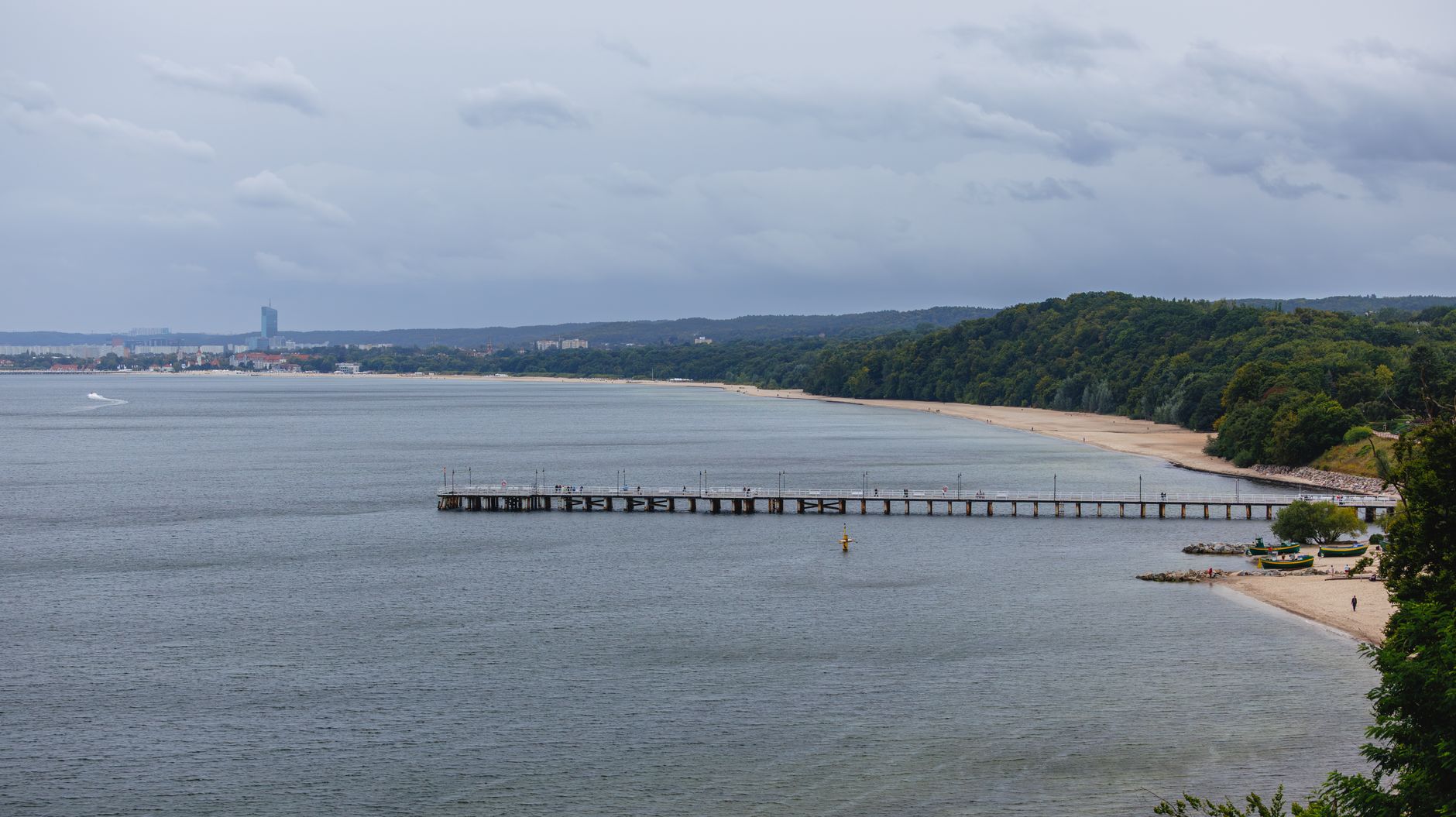Tranquil seascape with a long pier extending into the ocean, flanked by lush greenery.